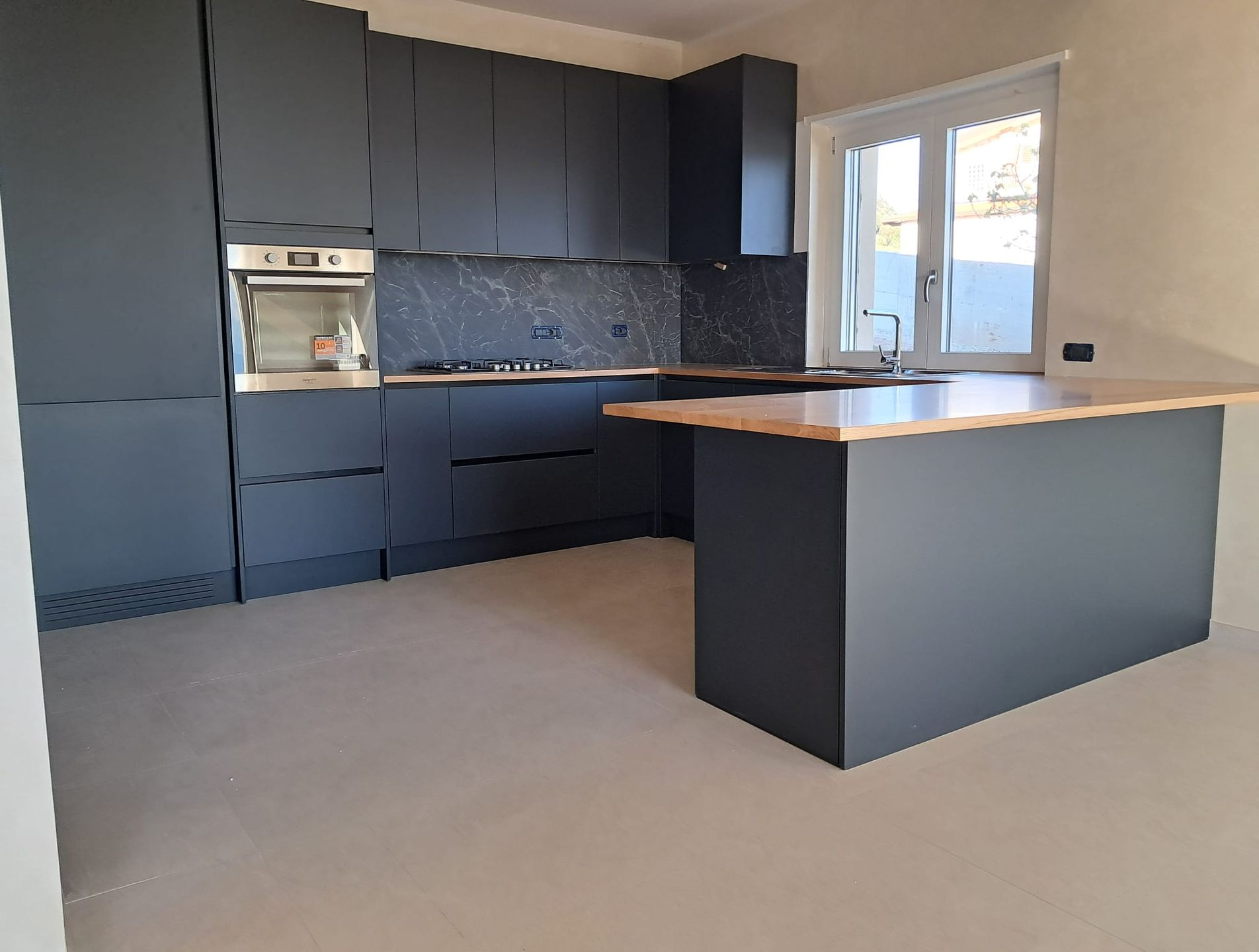 Una cucina moderna con mobili grigio chiaro, elettrodomestici in acciaio inossidabile, pavimento piastrellato e un'isola in pietra screziata.