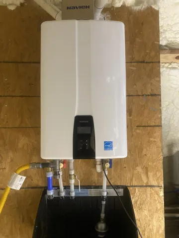 White wall-mounted water heater with pipes and gas line in a utility space