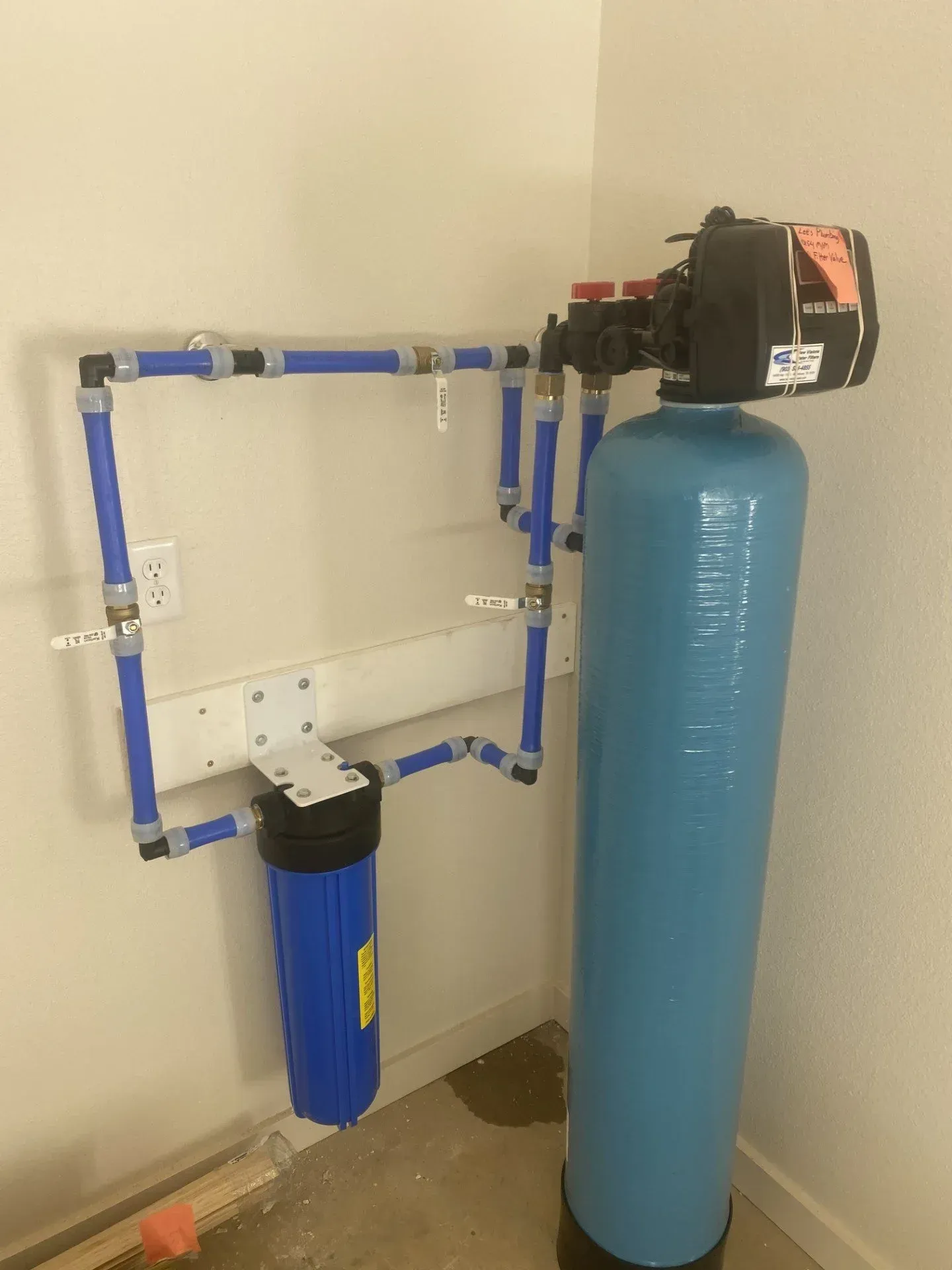 Blue water filtration system with pipes, tank, and wall-mounted components in a utility room