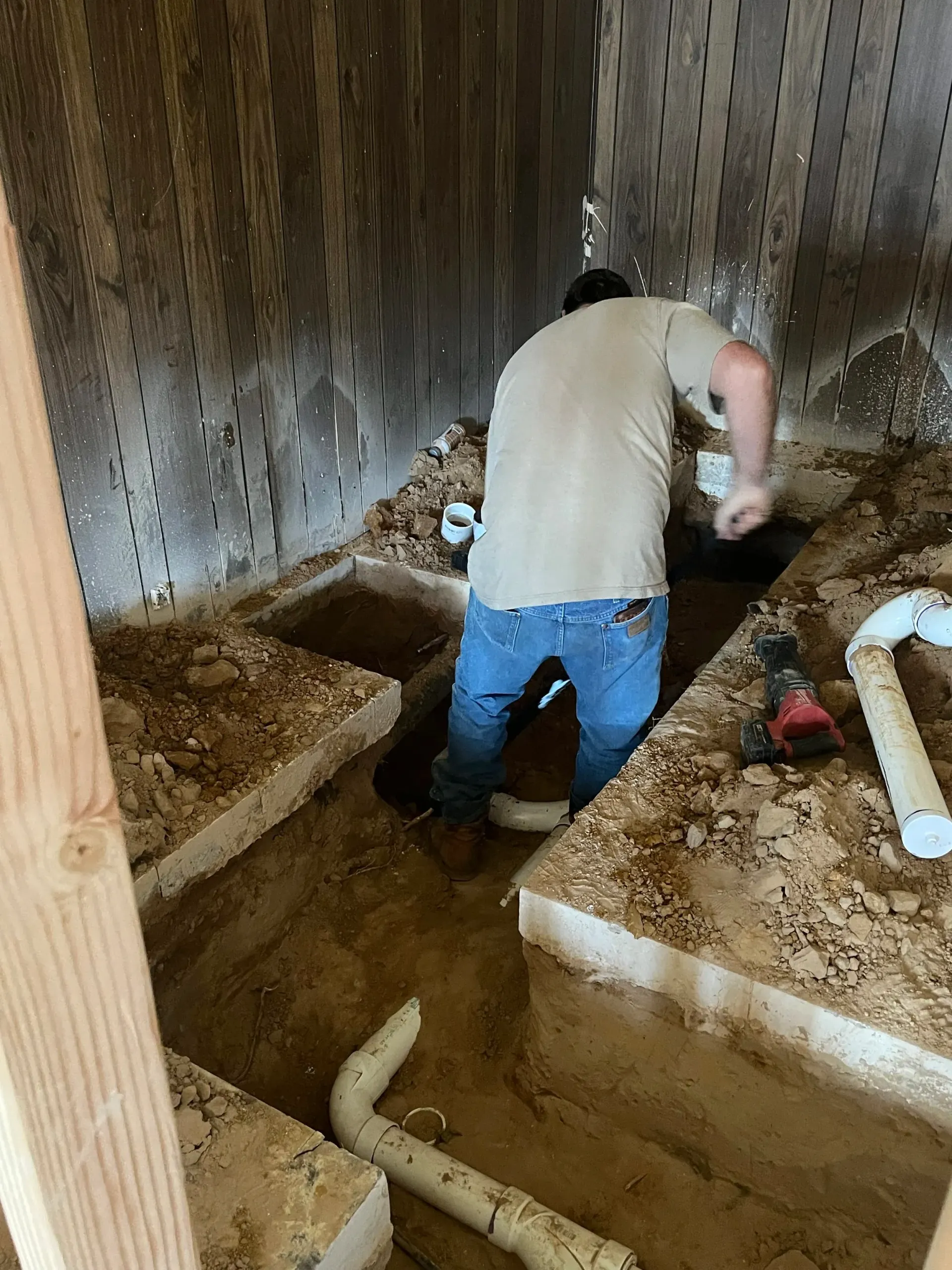Person working in a narrow dirt trench beside concrete footings inside a construction or excavation site