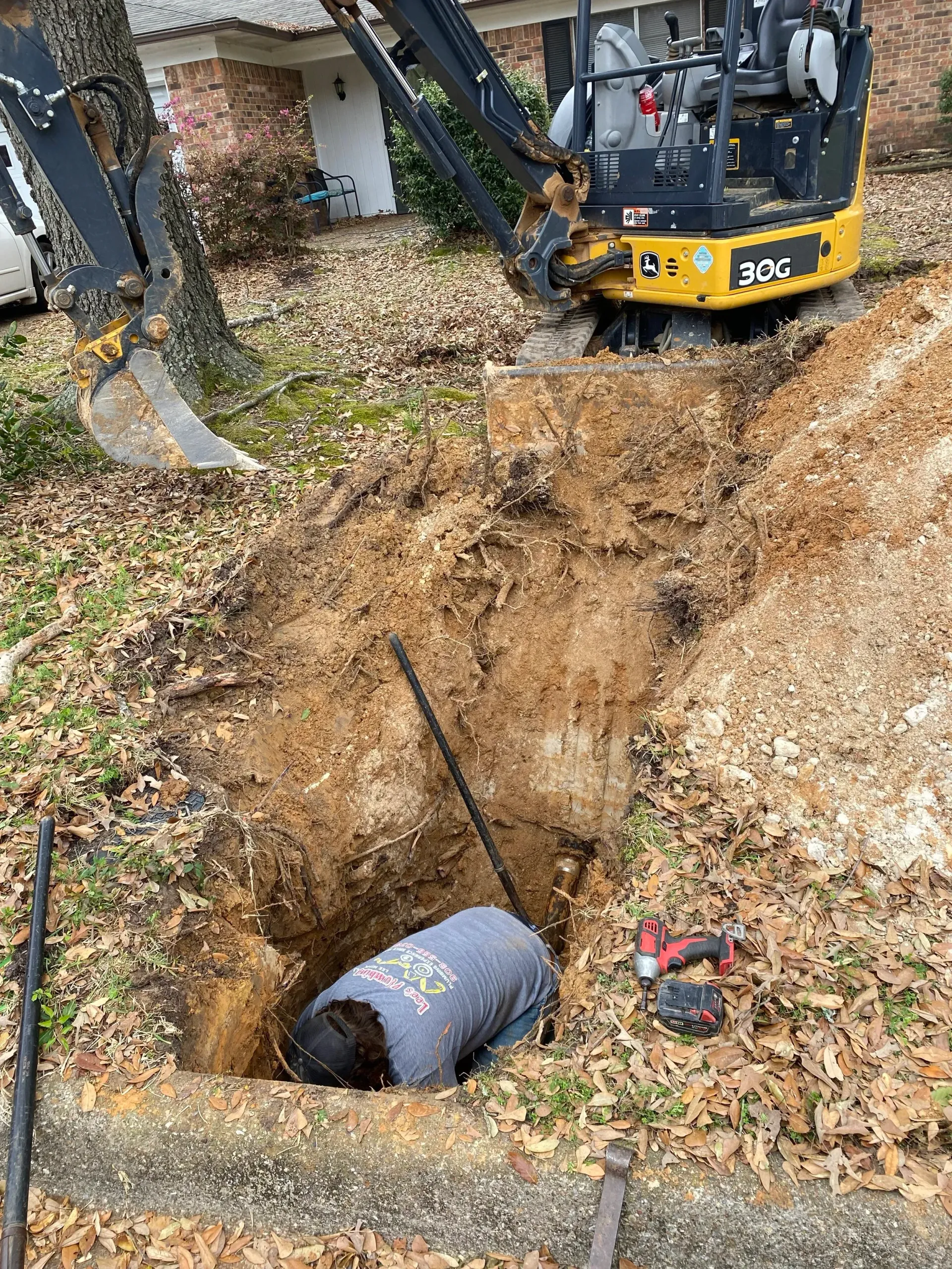Mini excavator digging a trench beside a house; large dirt pit with a pipe exposed in the foreground.