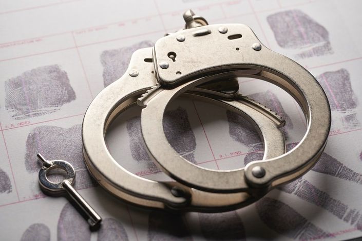 A pair of handcuffs and a key on top of a piece of paper with fingerprints.