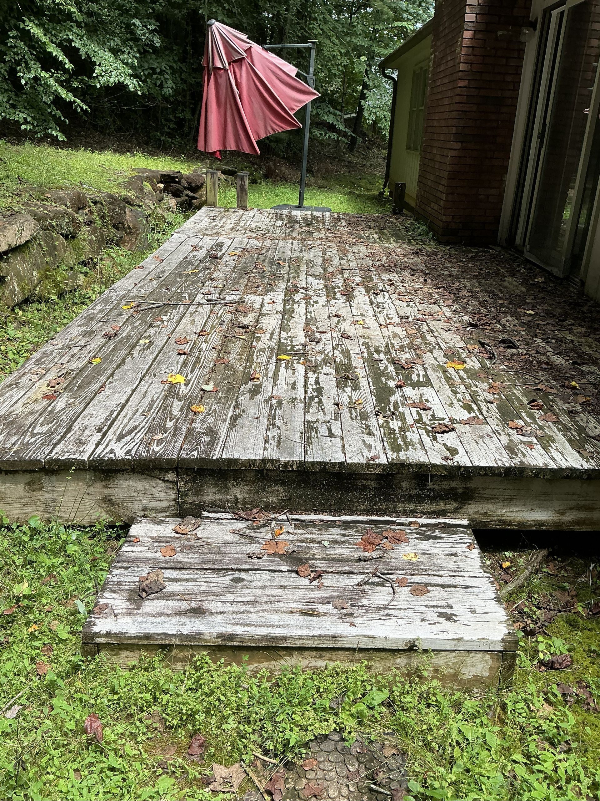 Weathered wooden deck with peeling white paint, steps, and a red umbrella in a grassy yard.