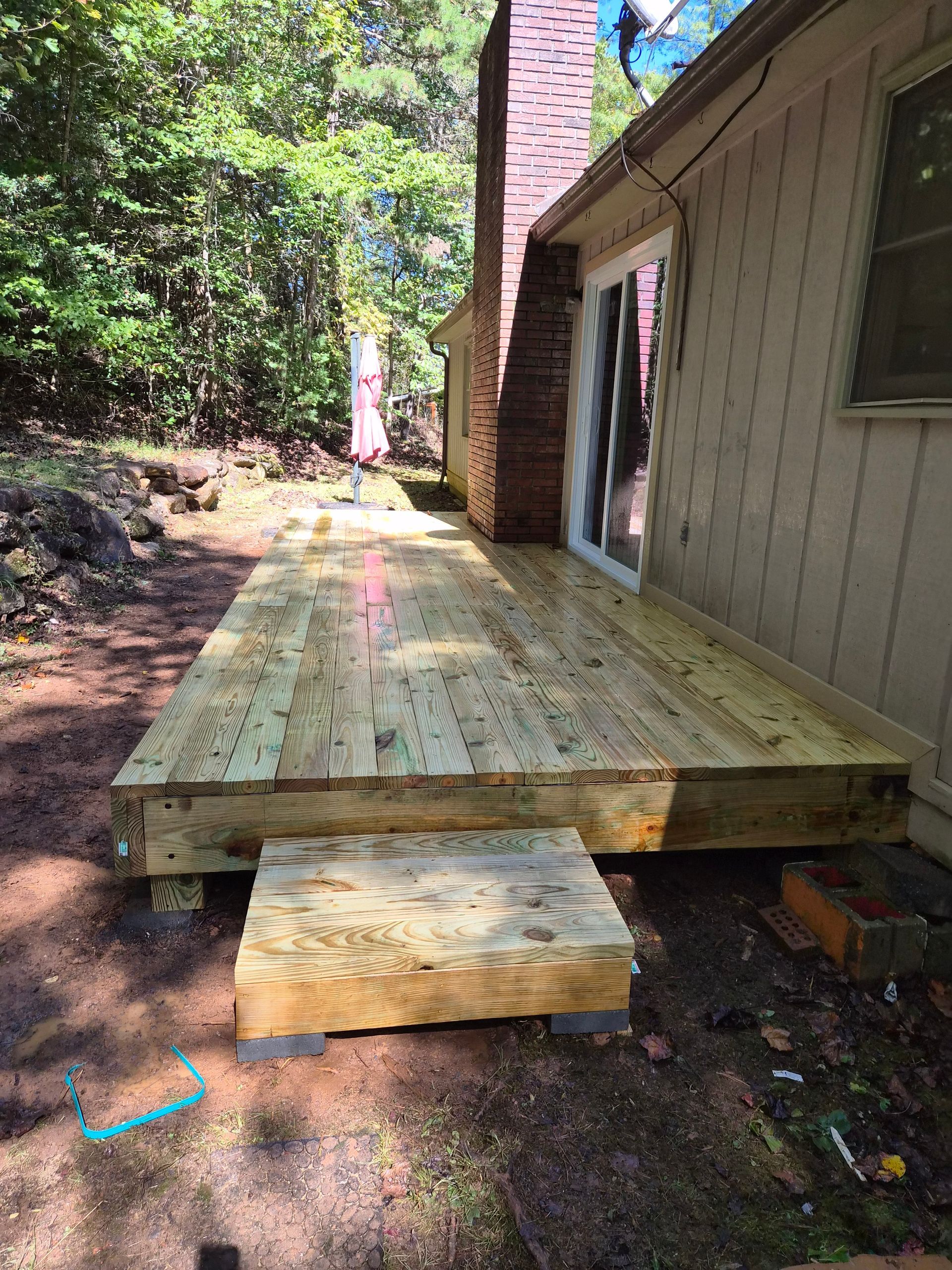Newly built wooden deck with a step, next to a house with a chimney and a sliding glass door.