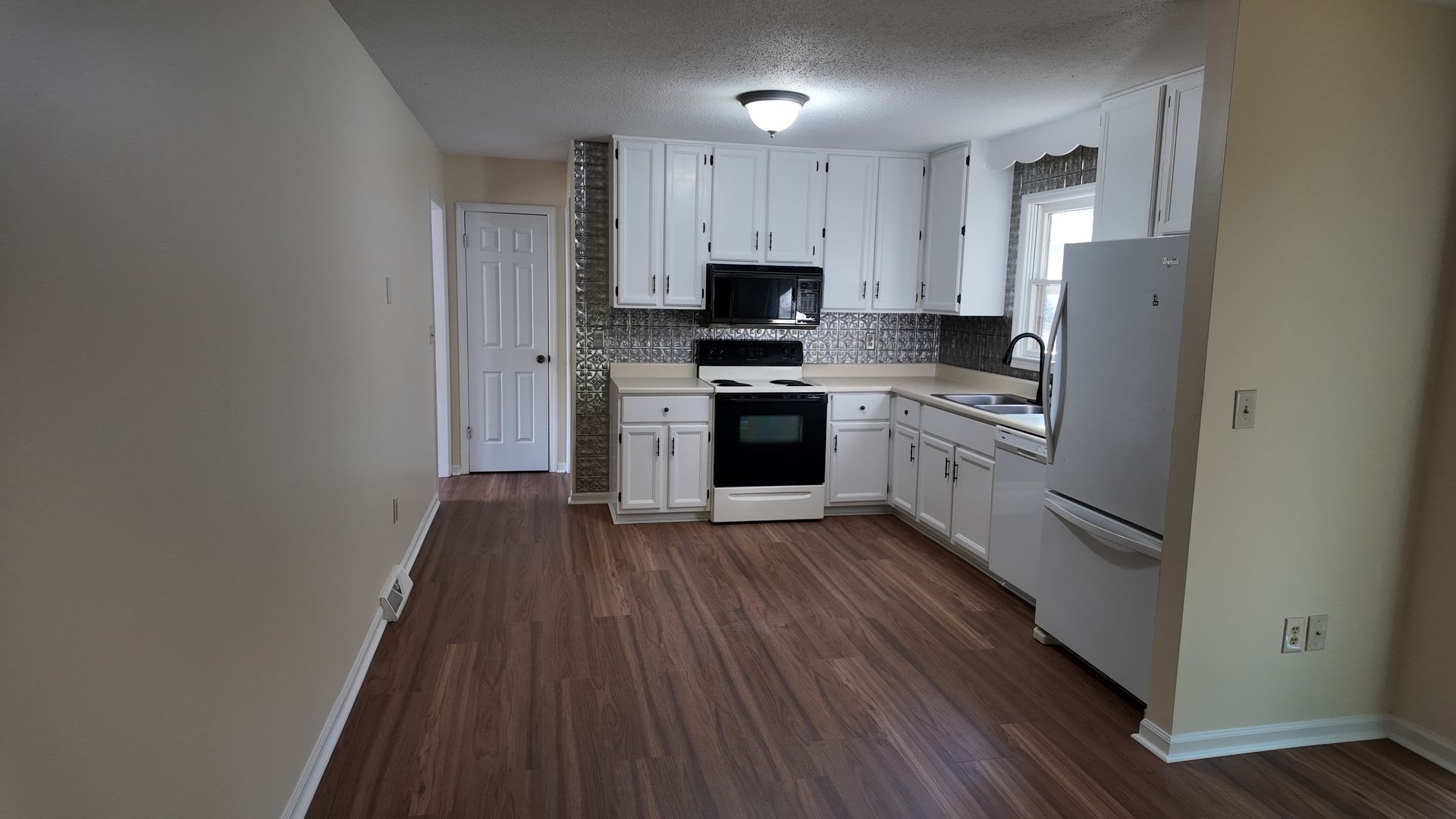 Kitchen with white cabinets, appliances, dark wood-look floor, and a patterned backsplash.