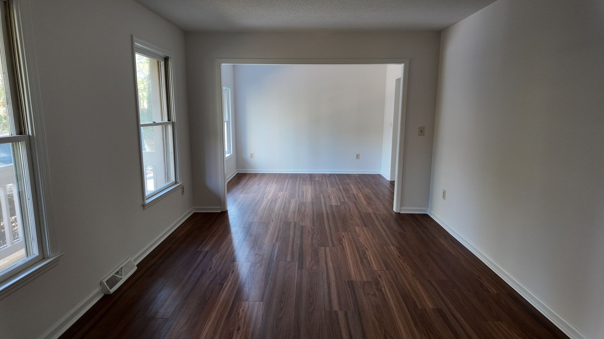 Empty room with hardwood floors, white walls, and an archway leading to another room.