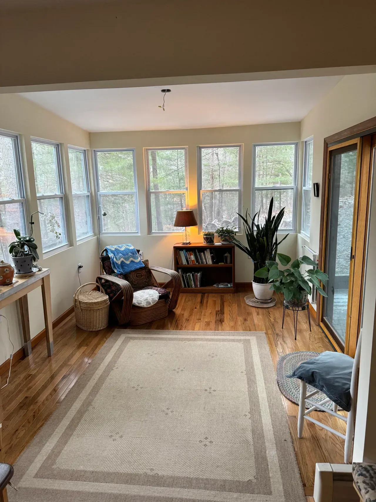 Sunroom with windows, hardwood floors, rug, chair, bookcase, and plants.