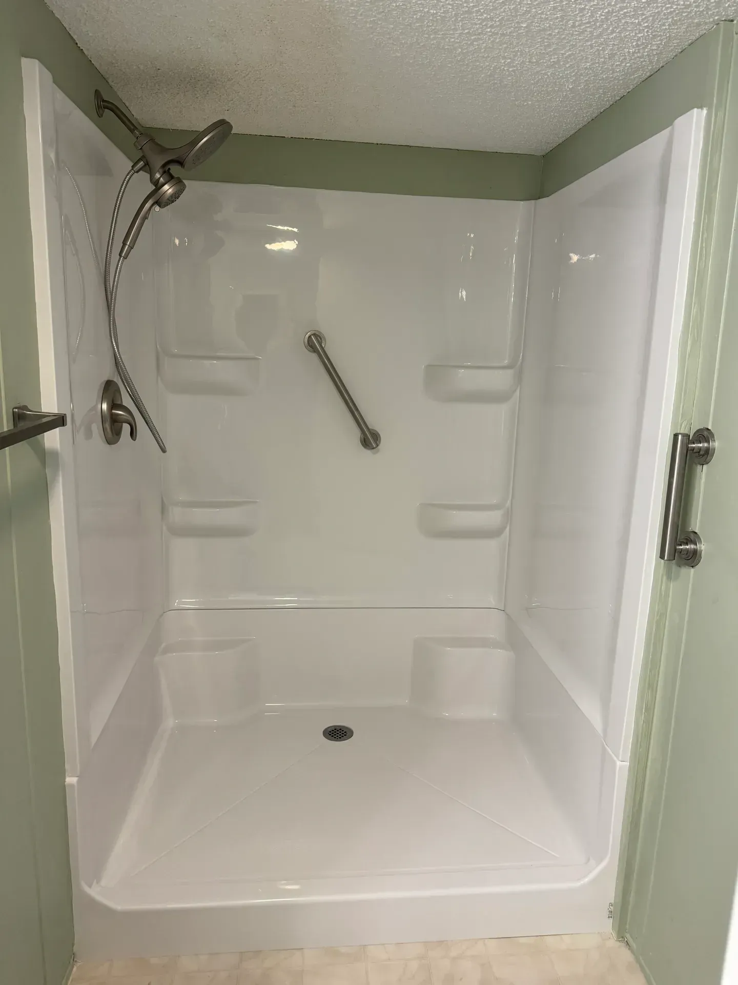 White accessible shower with grab bar, built-in shelves, and silver fixtures.