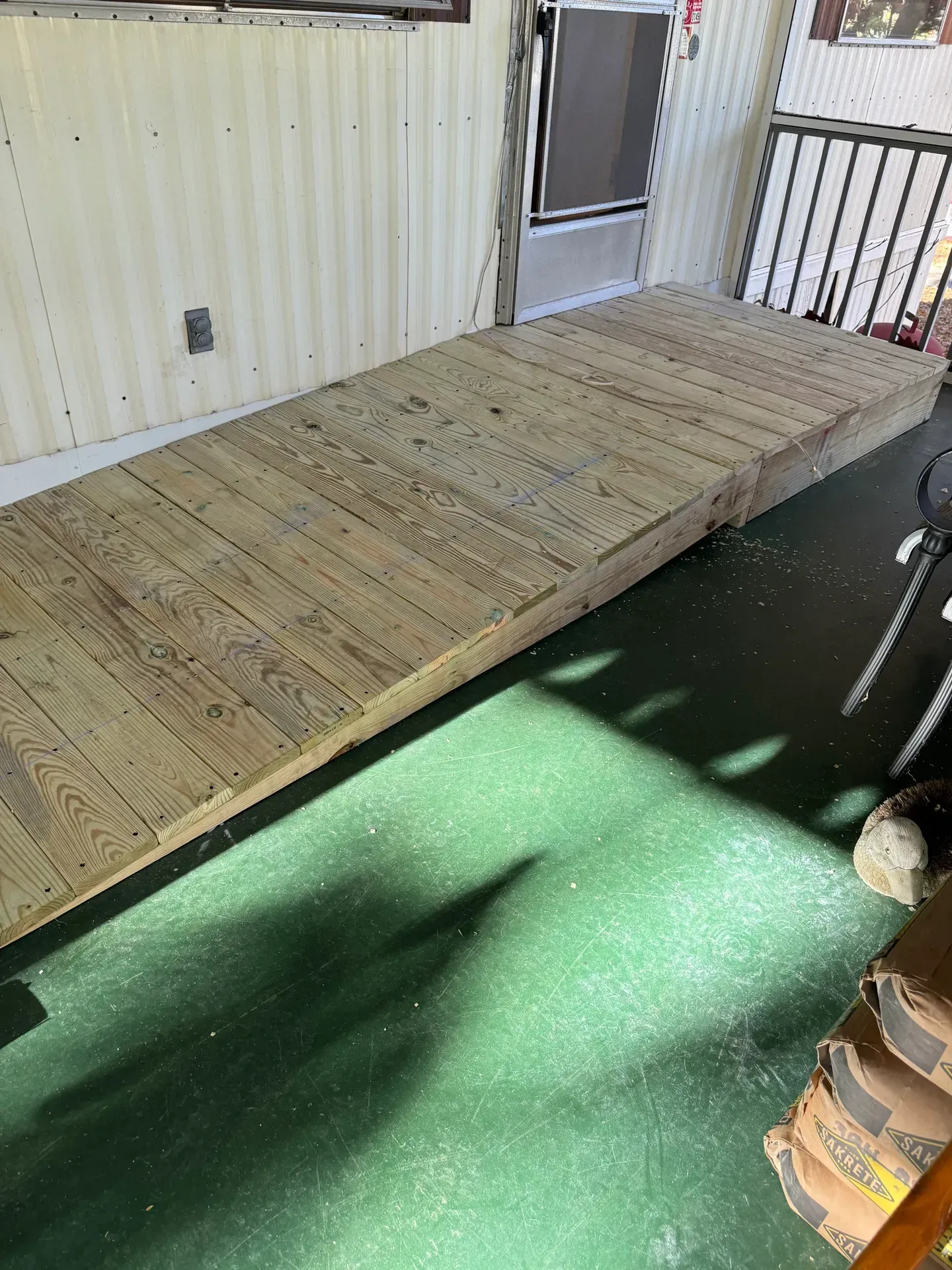 Wooden ramp leading to a doorway. The ramp is light brown, set on a green floor. White siding is visible.