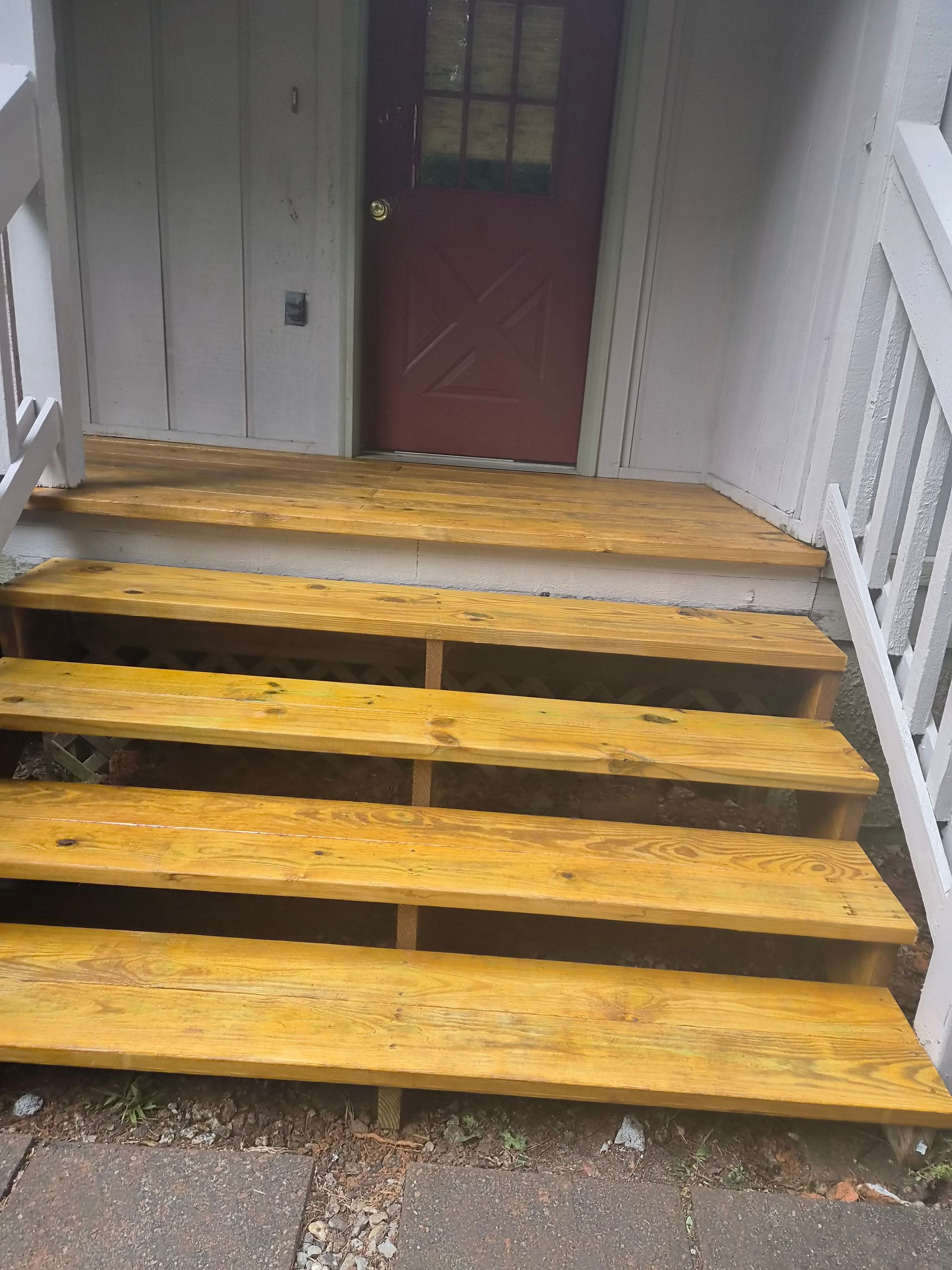 Wooden outdoor stairs leading to a red door, painted yellow, set against a white wall.