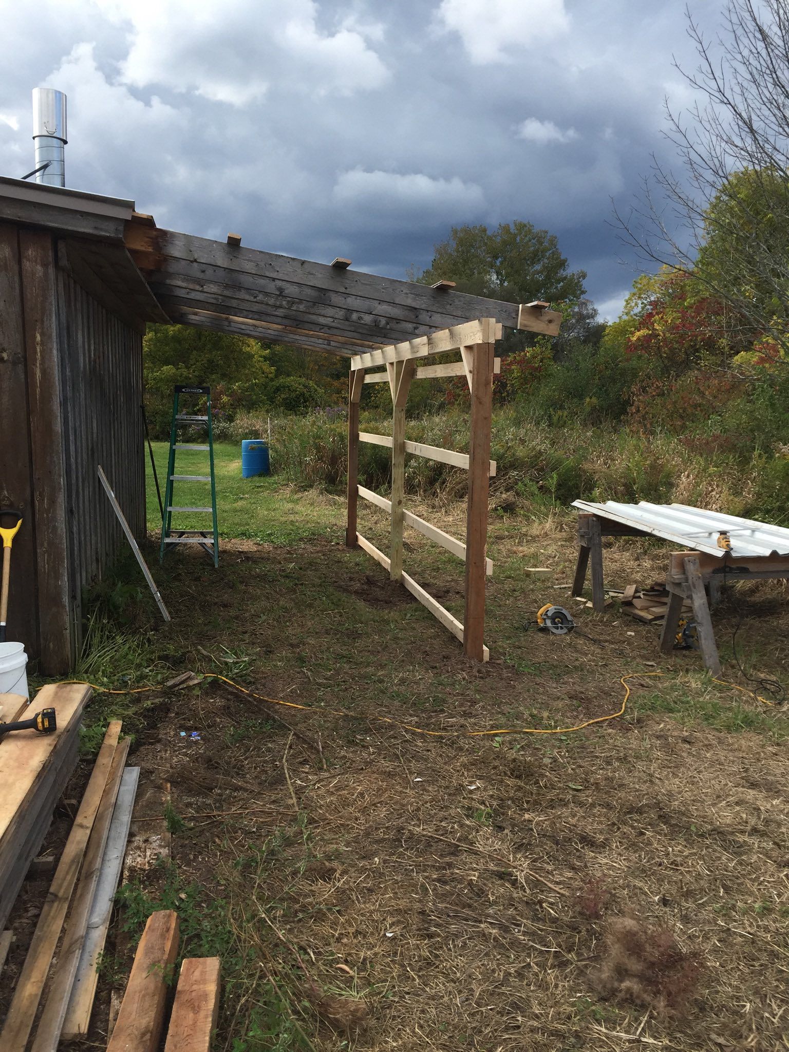 A wooden fence being built outside a weathered shed under a cloudy sky.
