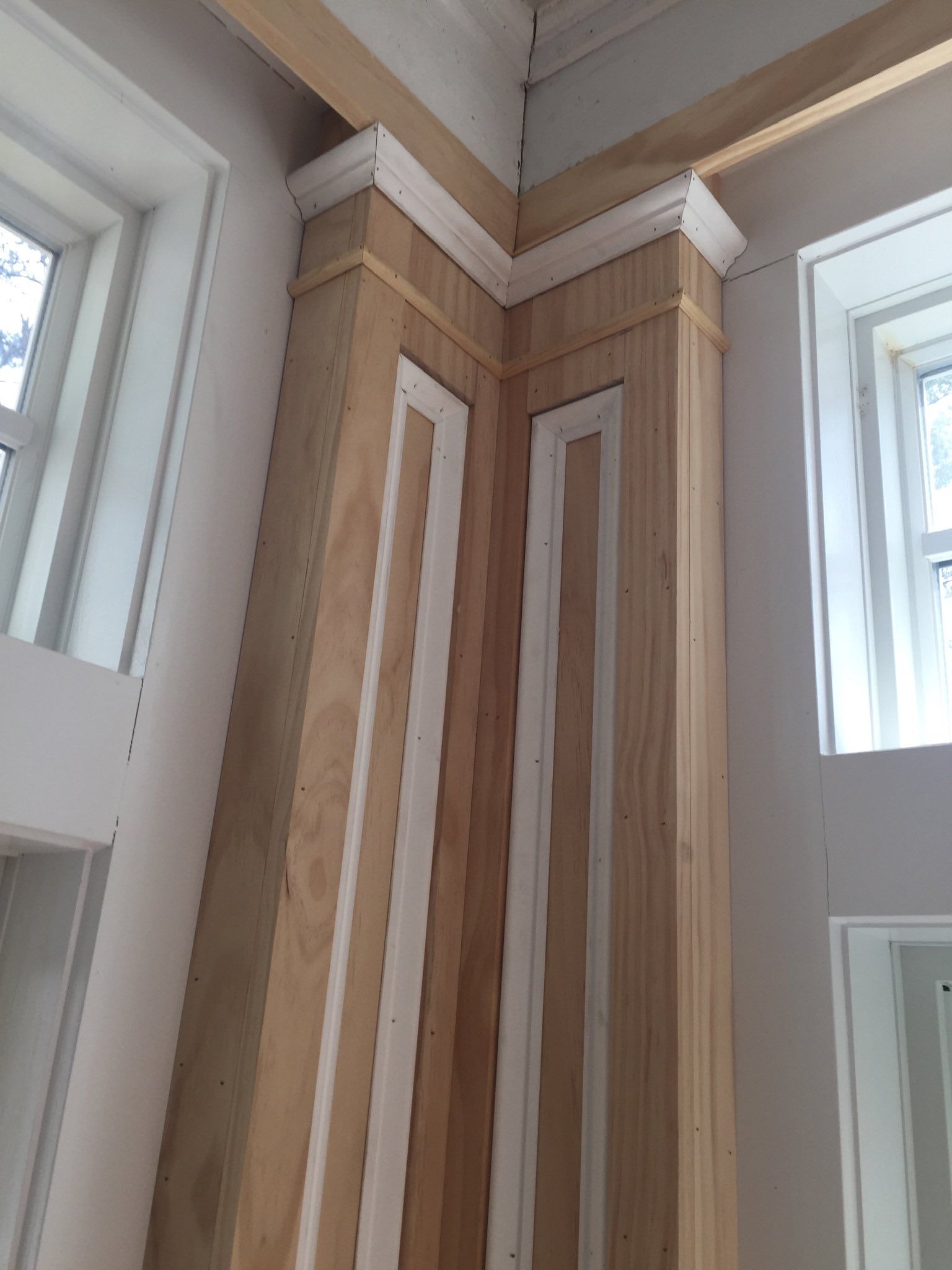 Corner of a room under construction with wooden trim and white accents around the windows.