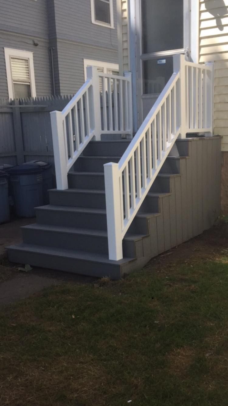 Grey outdoor stairs with white railings, leading up to a doorway.