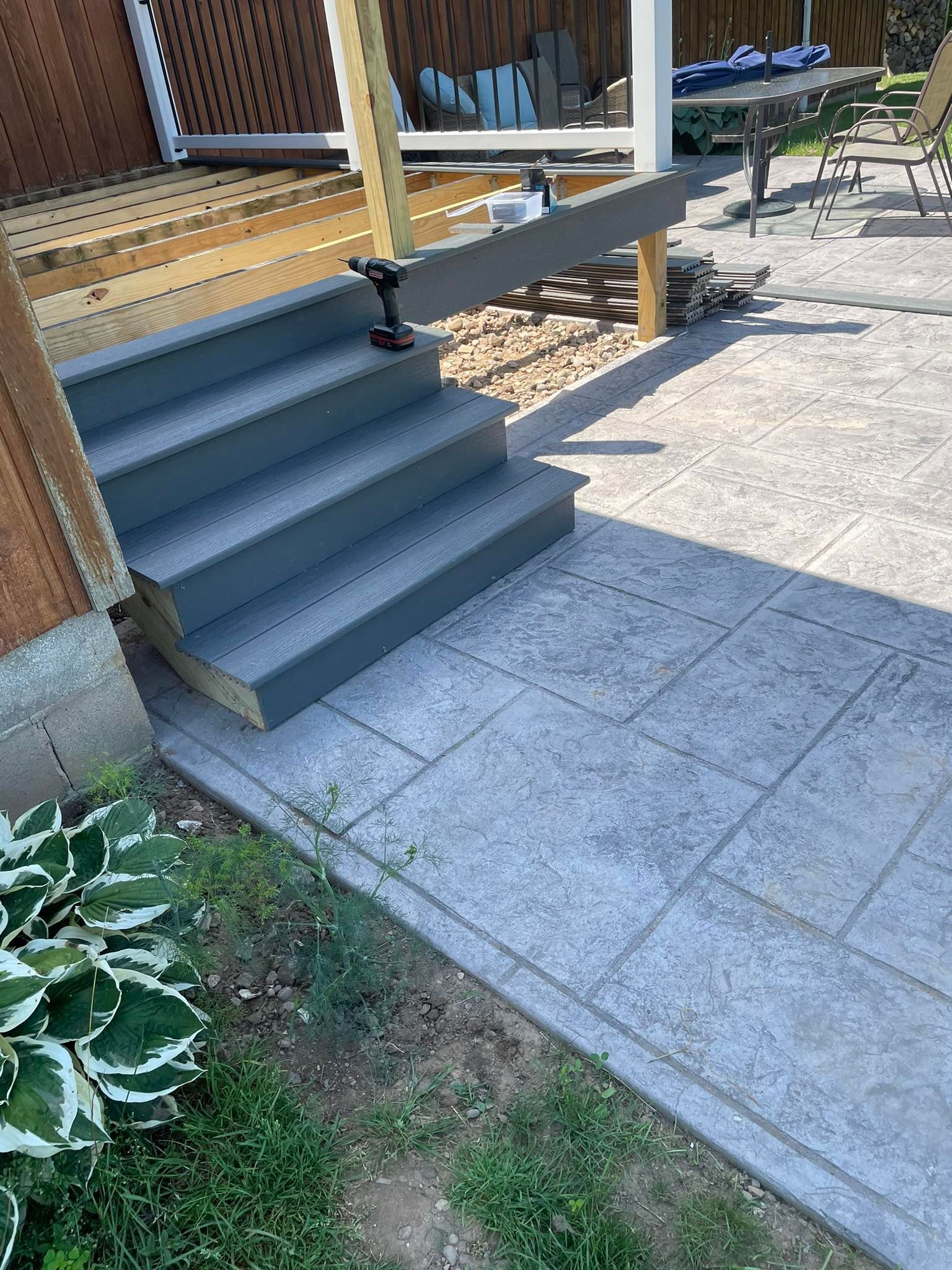 Gray deck steps leading down to stamped concrete patio.
