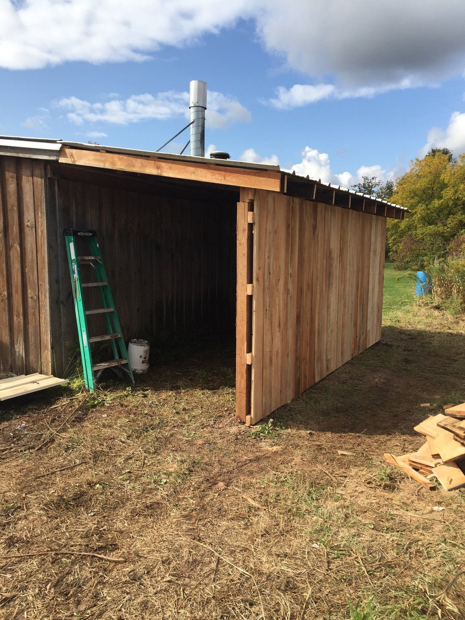 Wooden shed with an open side, ladder, and paint can. Sunny outdoor setting.