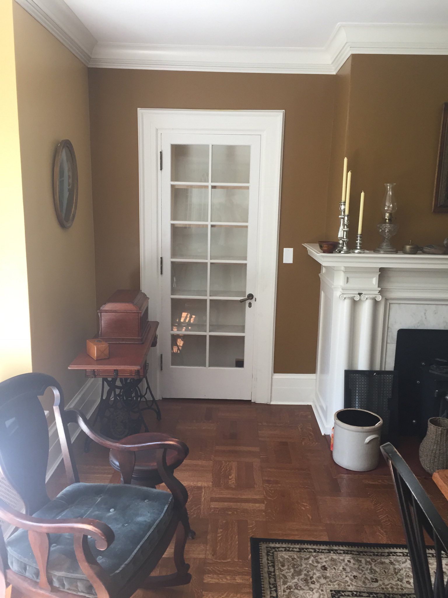A room with a door, fireplace, wood floor, and antique furniture. Walls are tan and brown.