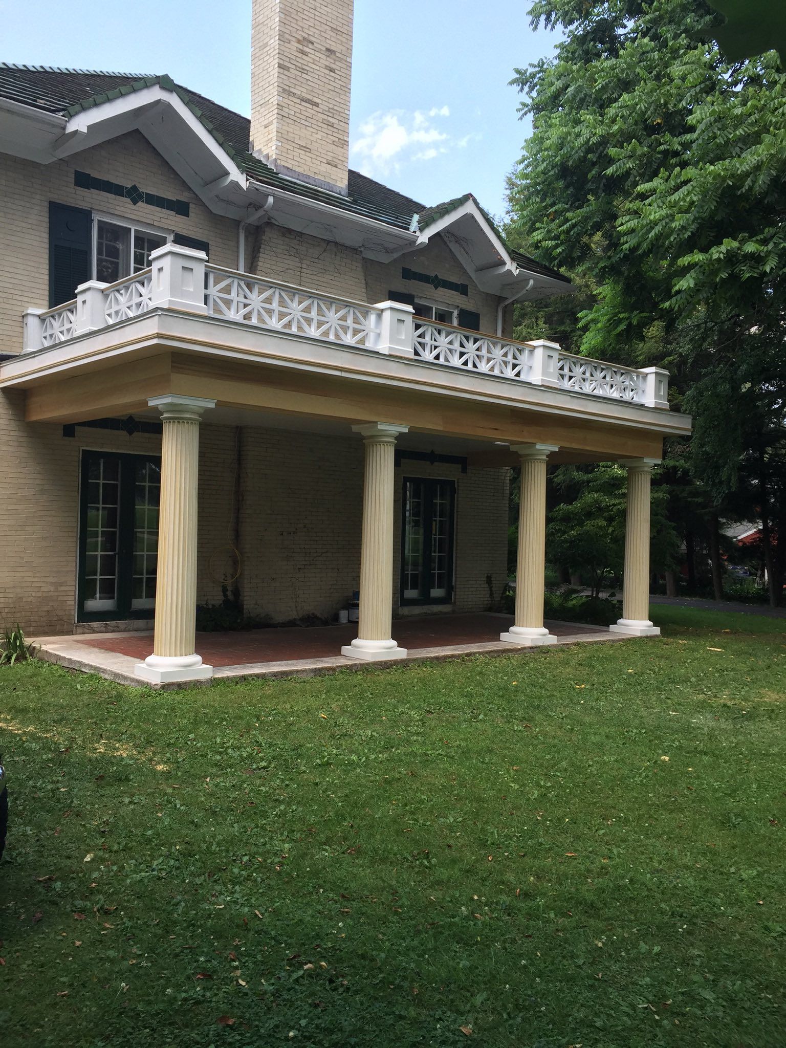 Two-story beige house with a balcony supported by columns, on a grassy lawn.