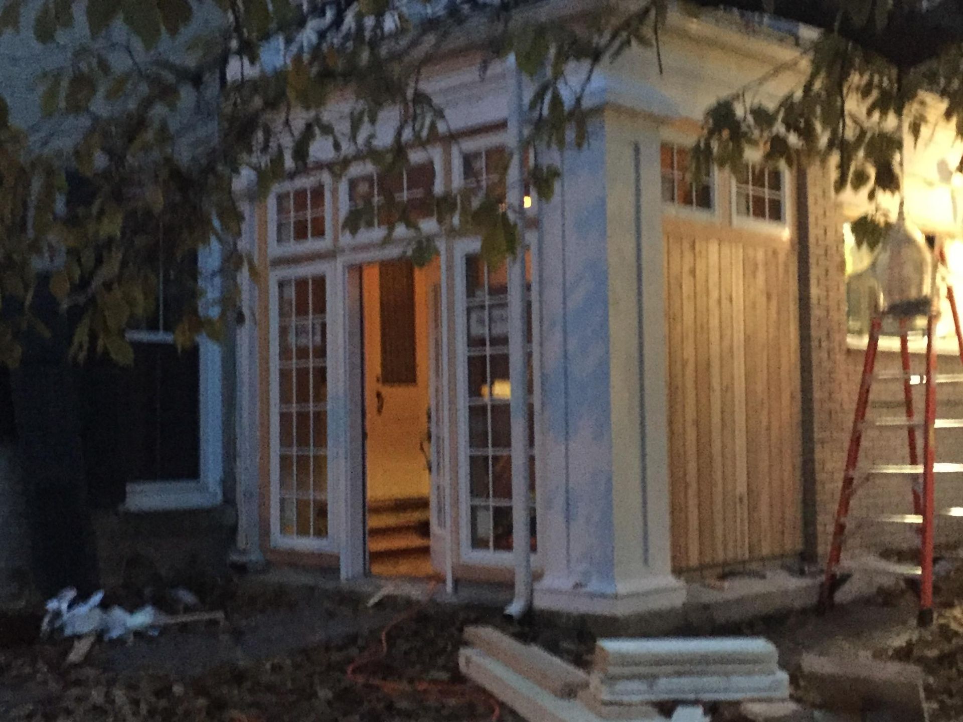 Exterior view of a building with open glass doors and wooden siding, construction in progress, evening.