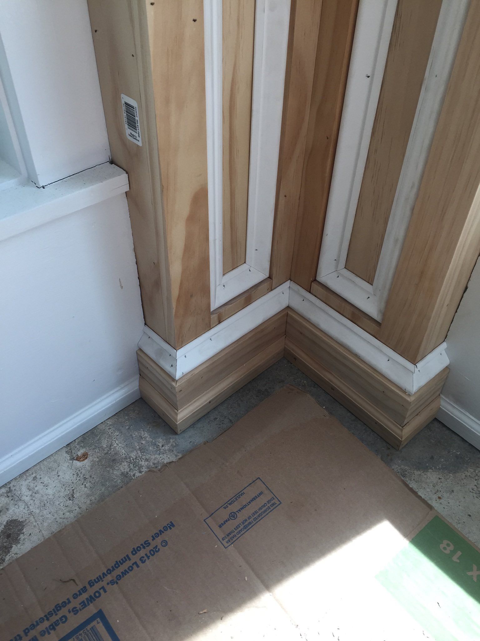 Corner of a room under construction, featuring wood trim and white molding on plywood walls.