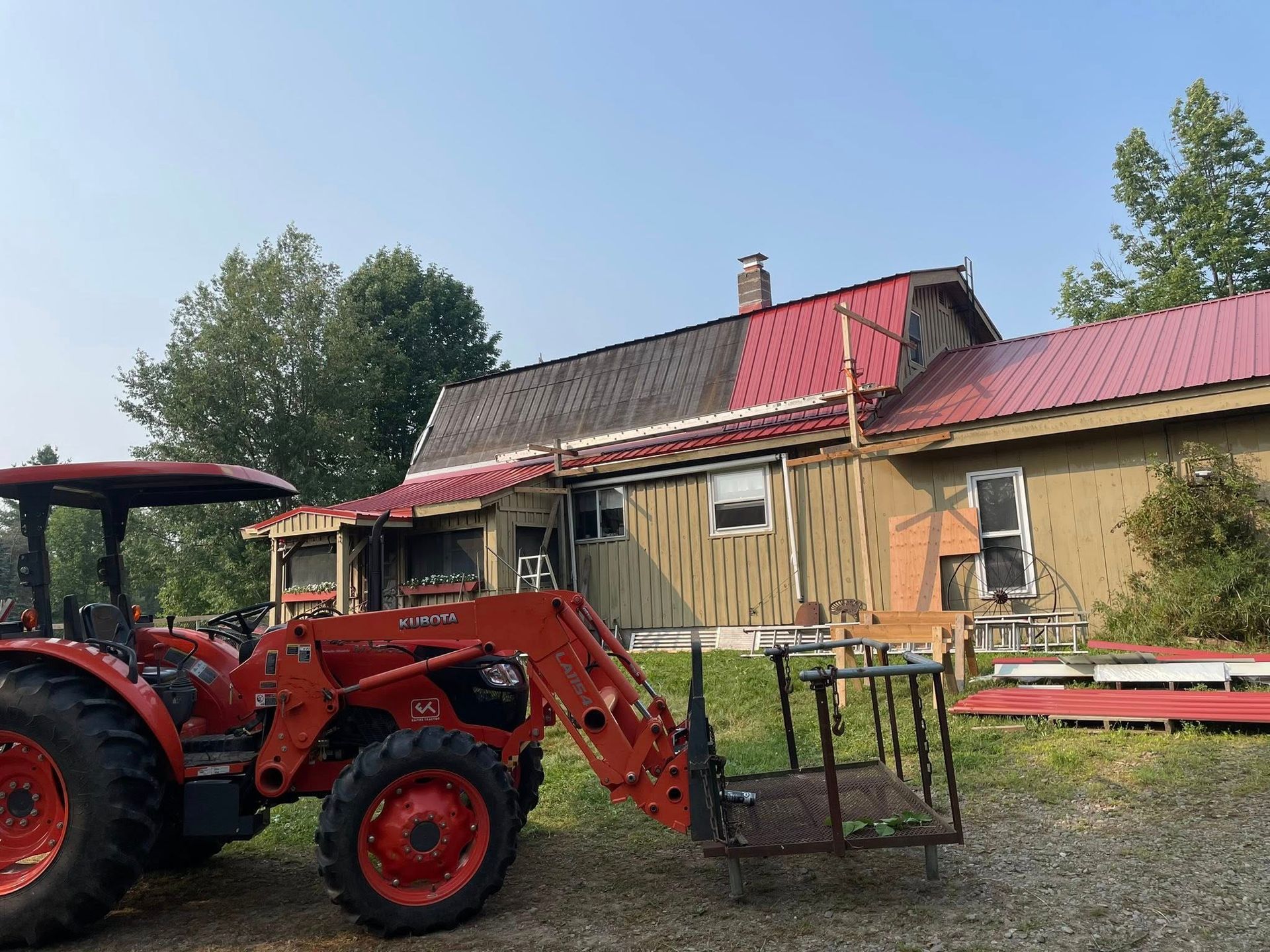 Orange tractor in front of a weathered house with a red roof, on a sunny day.