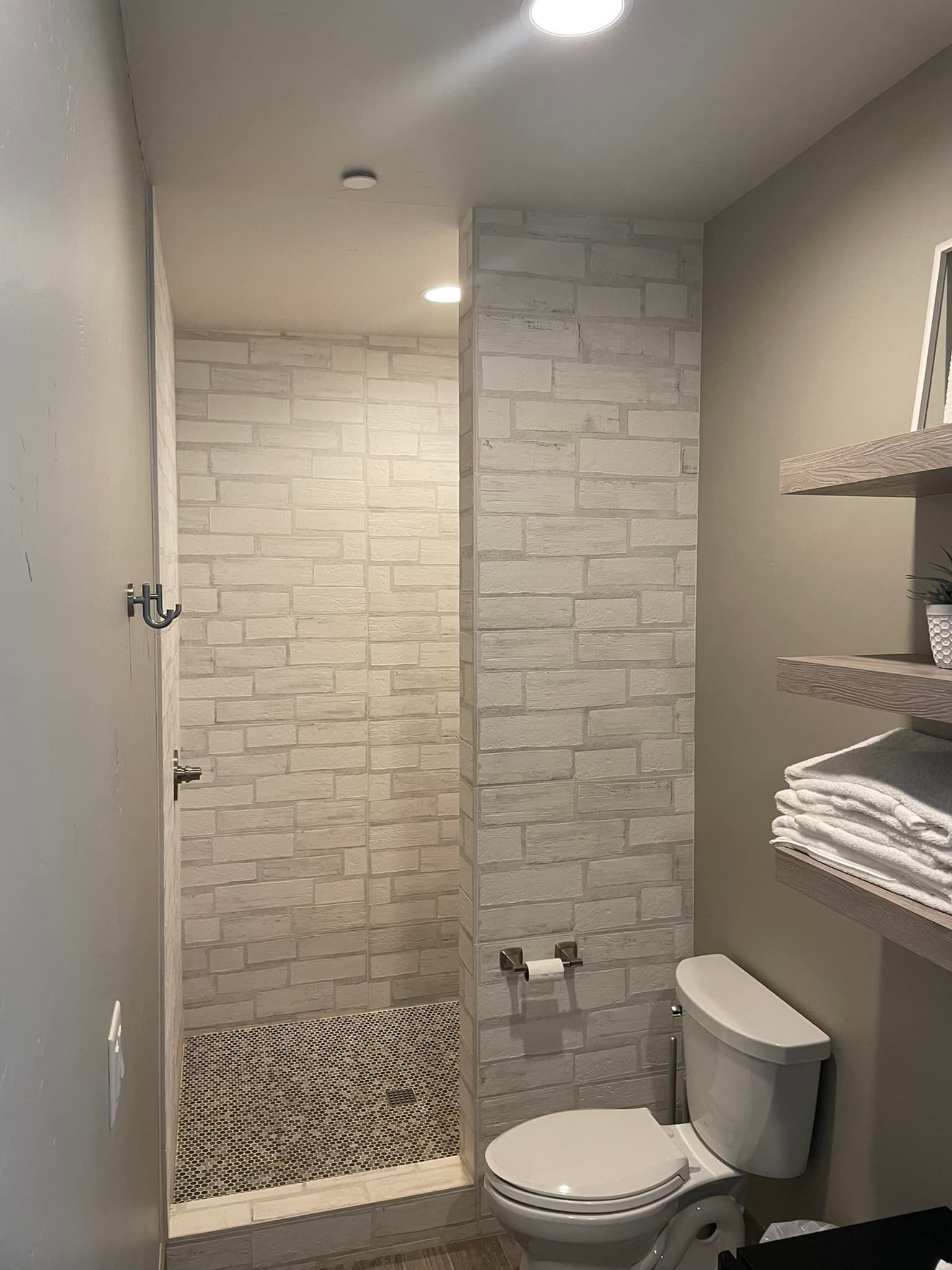 A bathroom with a toilet , shower and brick wall.