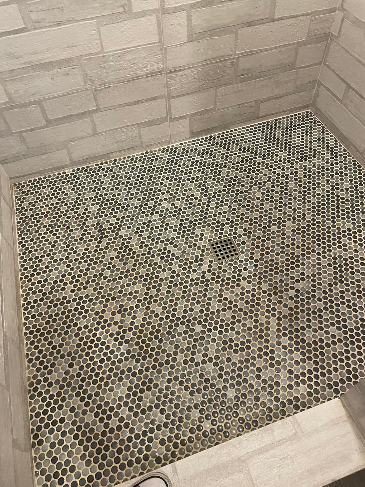 A shower with a black and white tile floor and a brick wall.