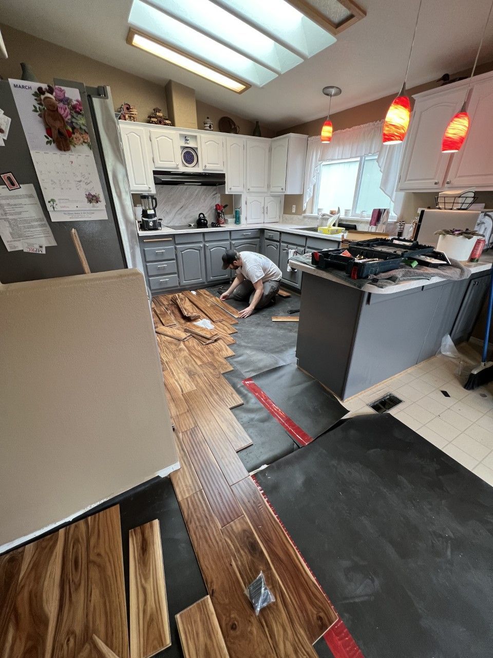 A man is laying wooden flooring in a kitchen.