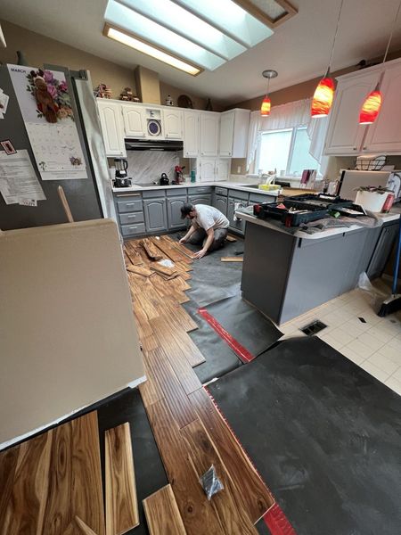A man is laying wooden flooring in a kitchen.