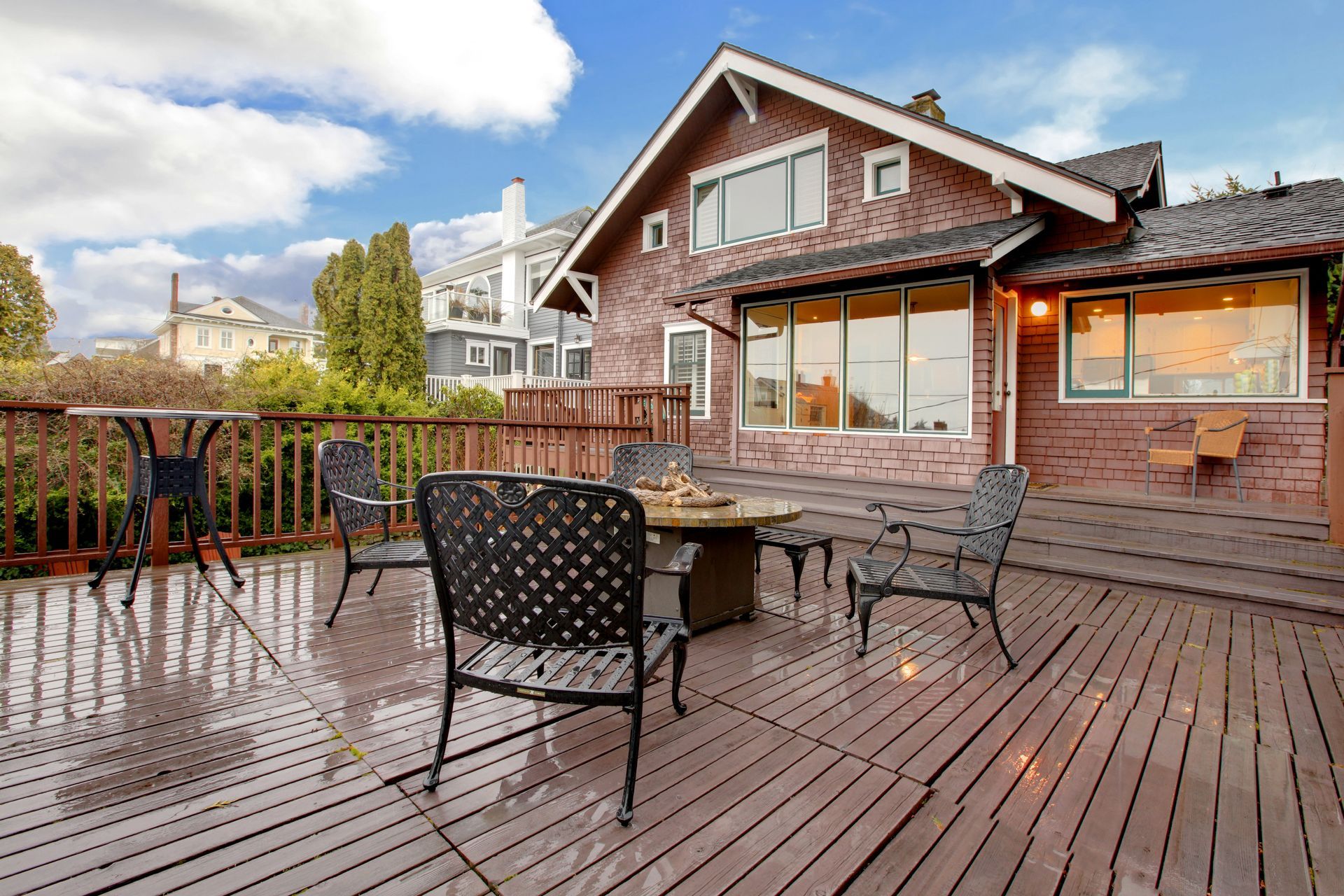 Wooden deck with outdoor seating in front of a brick house under a blue sky.