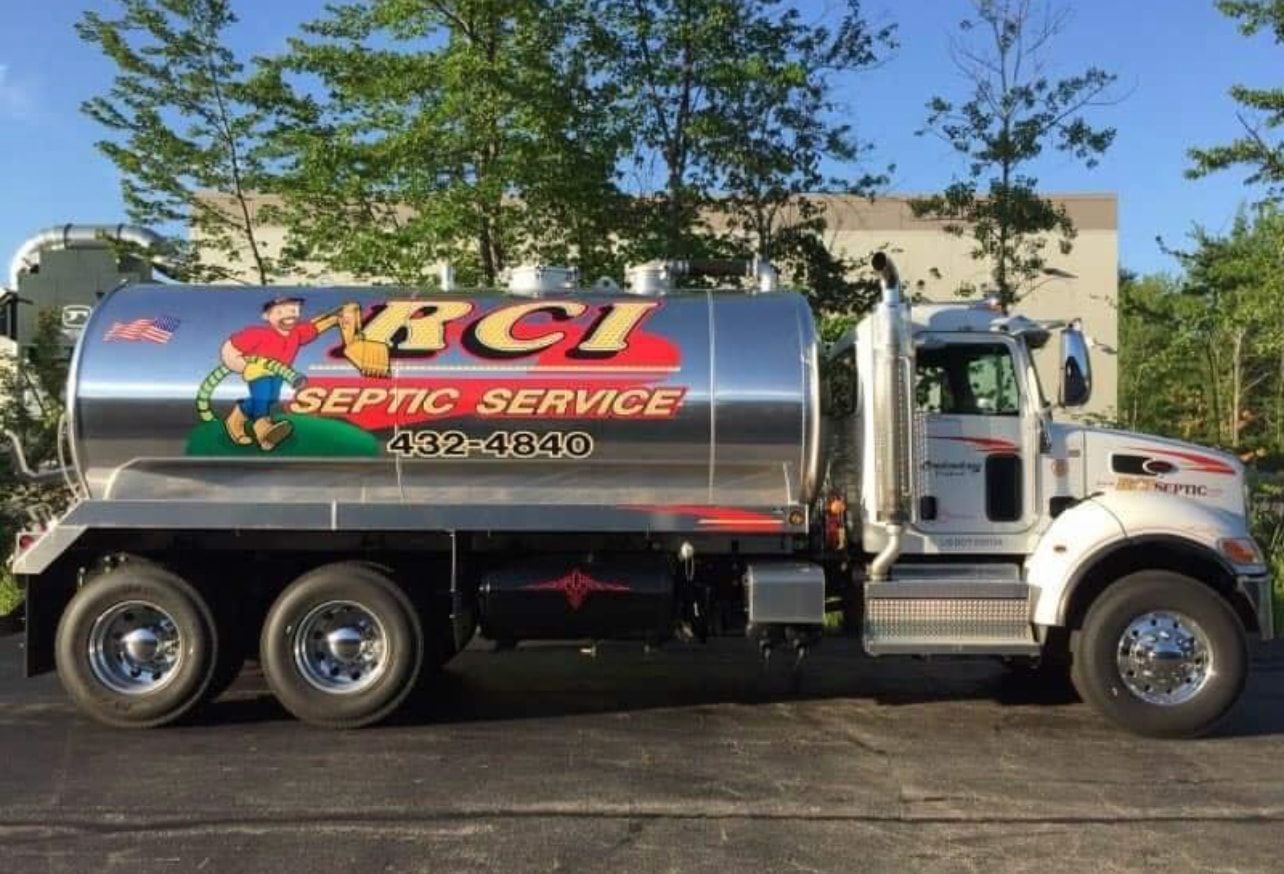Septic service truck with shiny silver tank, logo with a cartoon man, and contact info parked outside.