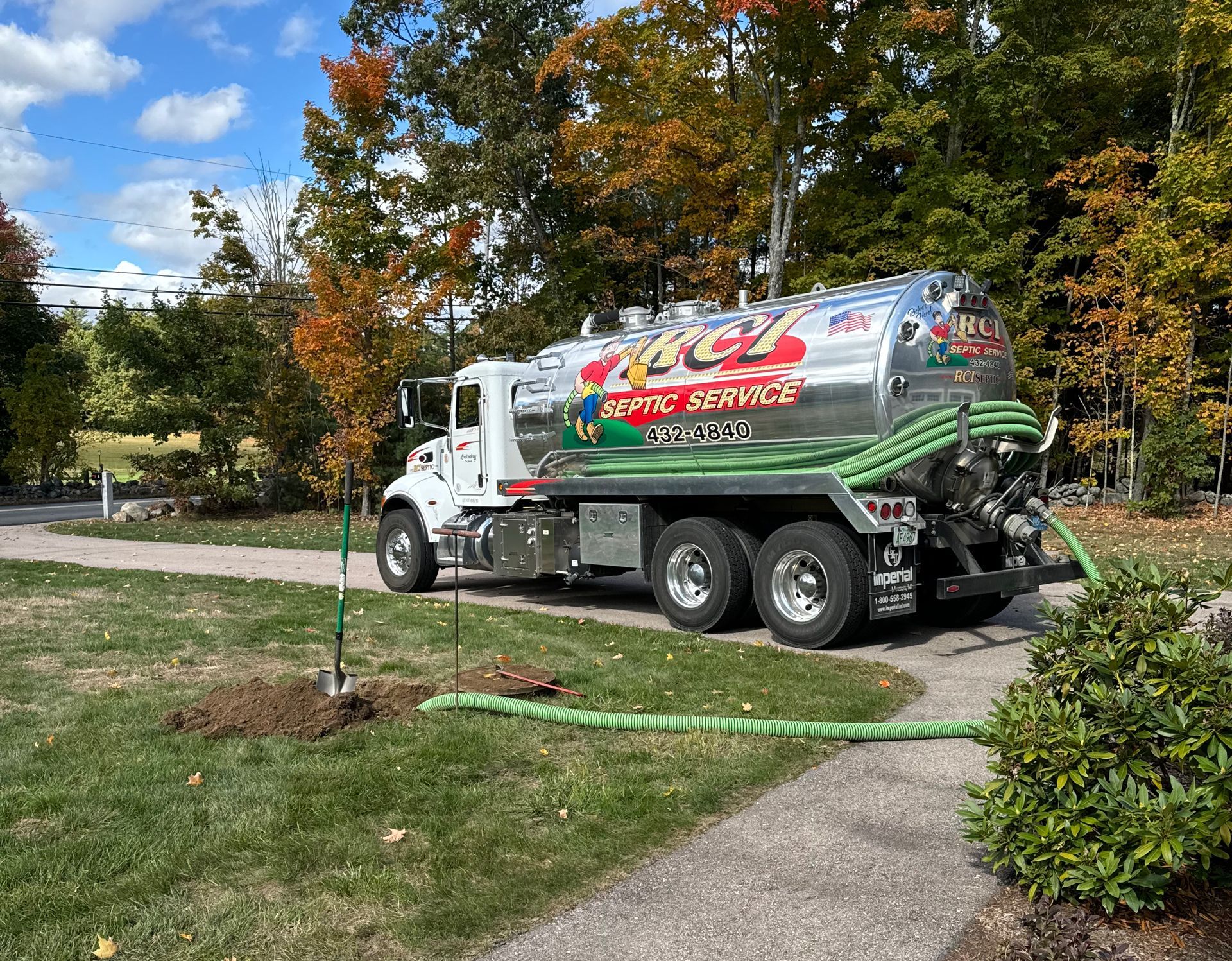 White tanker truck parked on a suburban street beside autumn trees and a sidewalk