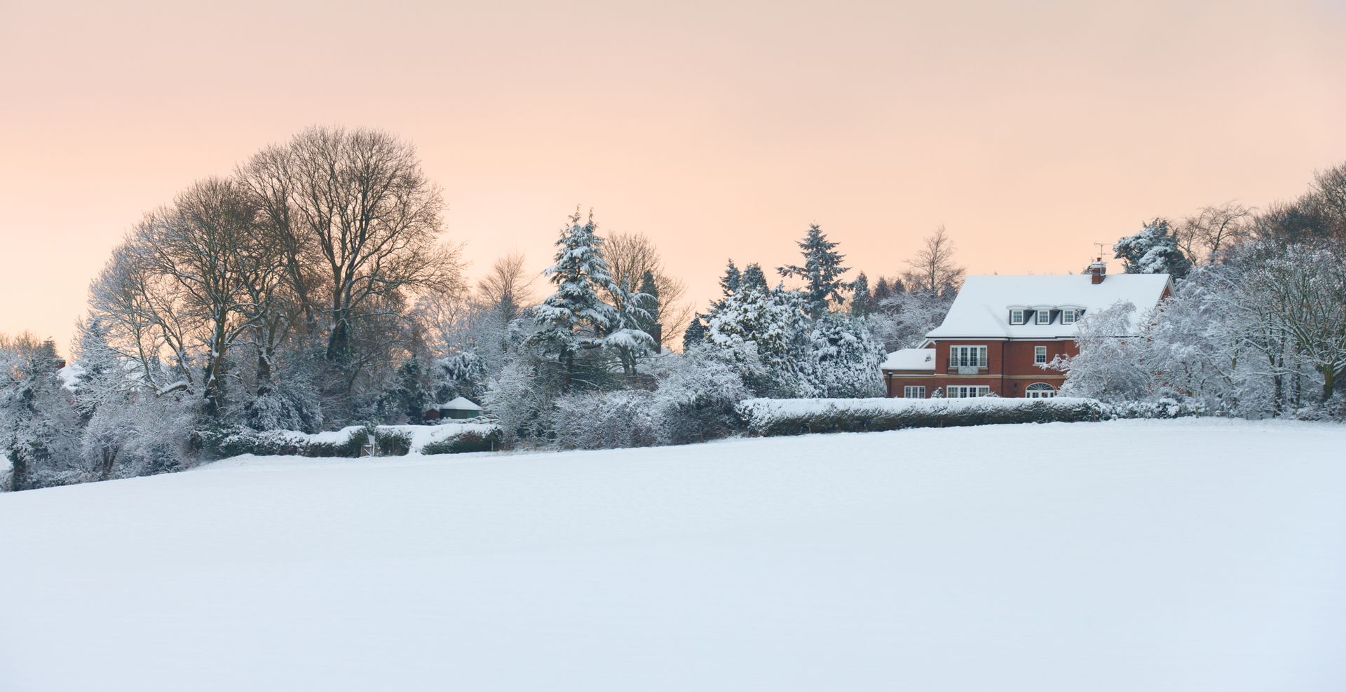 A red house is sitting in the middle of a snow covered field.