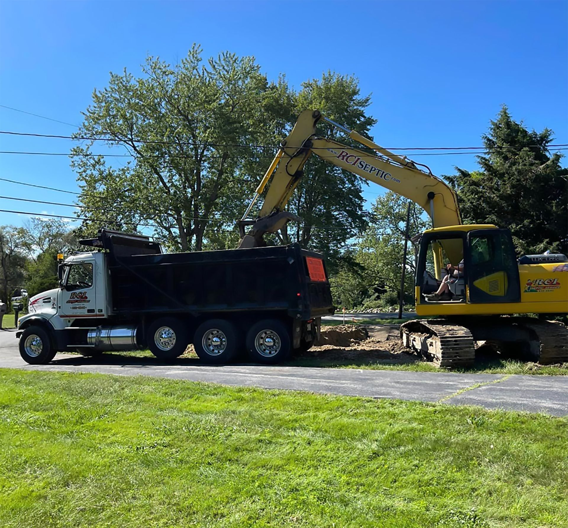 A dump truck is parked on the side of the road next to a yellow excavator