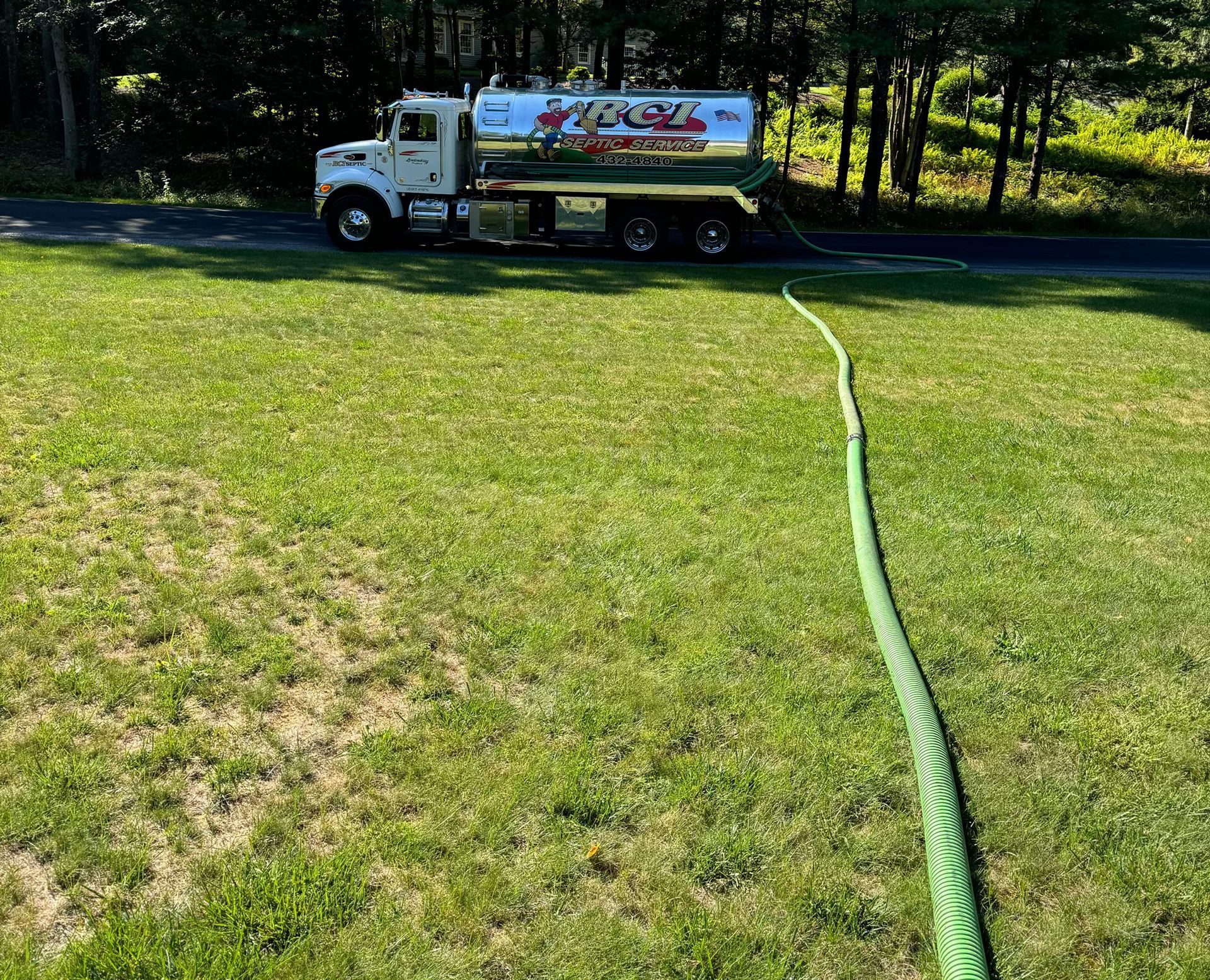 A white truck is parked in a grassy field with a green hose attached to it.