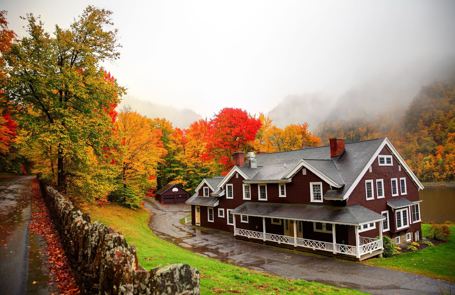 House with a brown exterior surrounded by vibrant fall foliage; misty mountains in the background.
