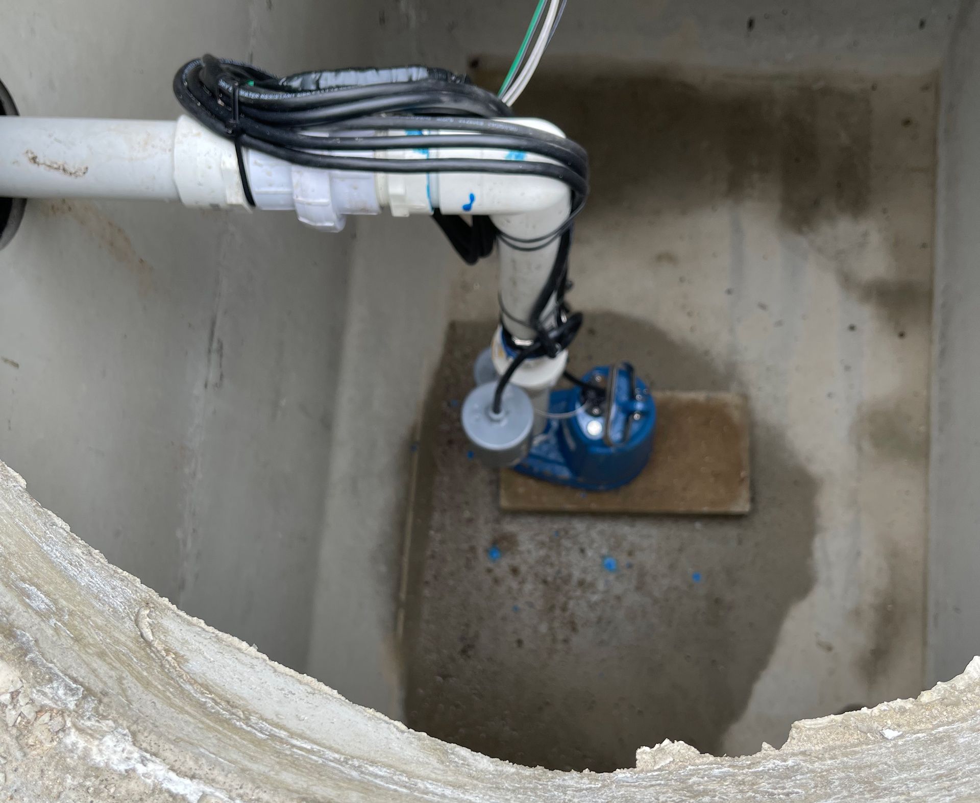 A blue septic pump is attached to a pipe in a hole