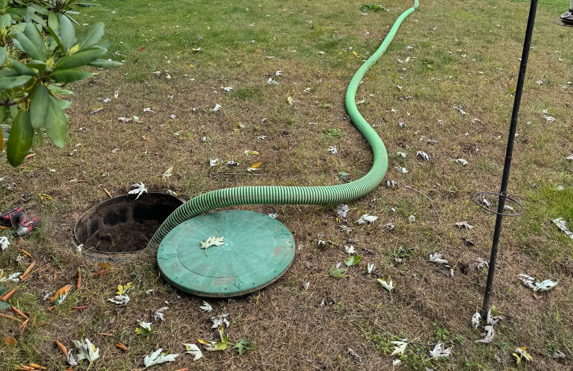 A green hose is coming out of a hole in the ground.