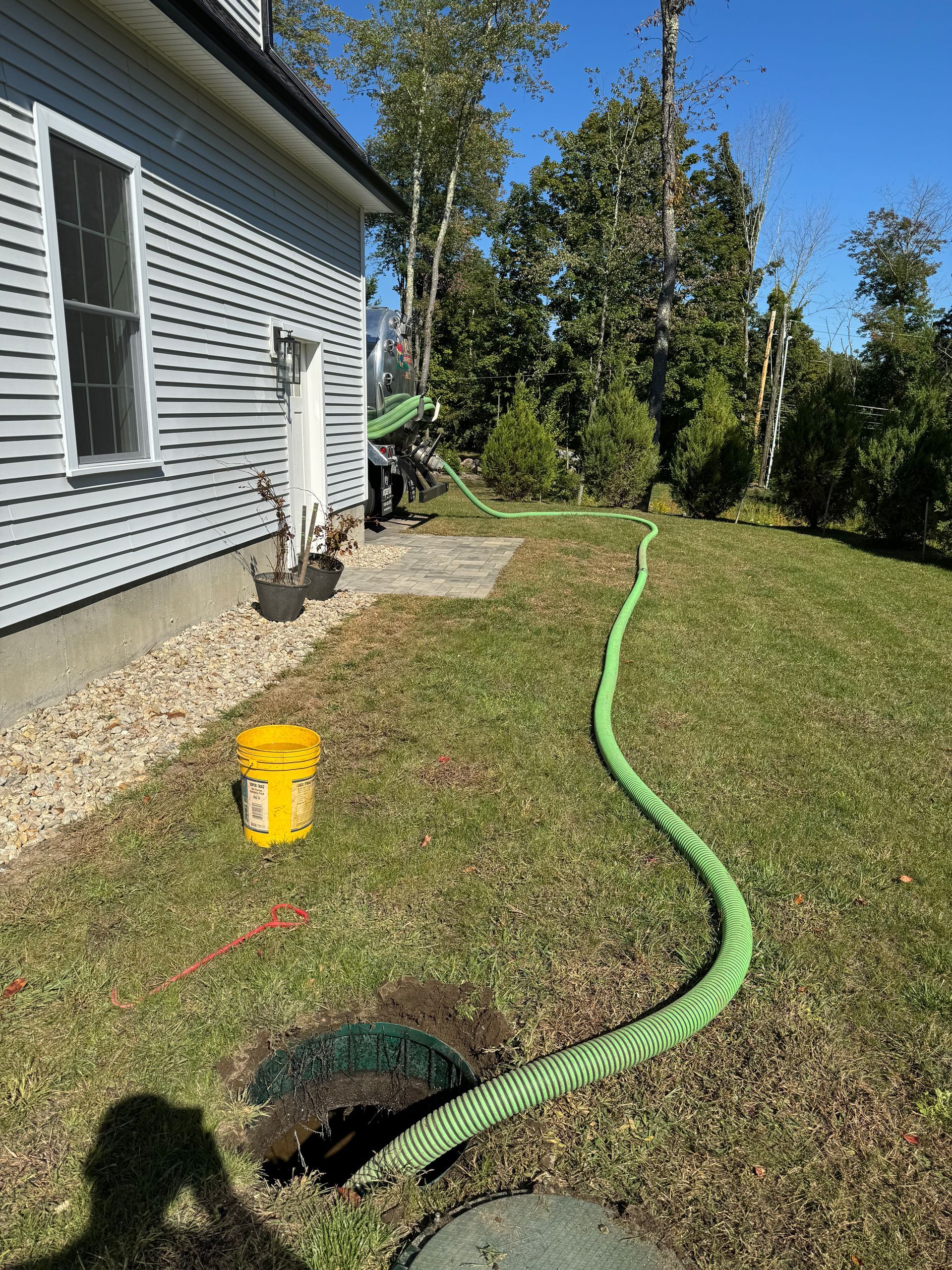 A green hose is connected to a septic tank next to a house.