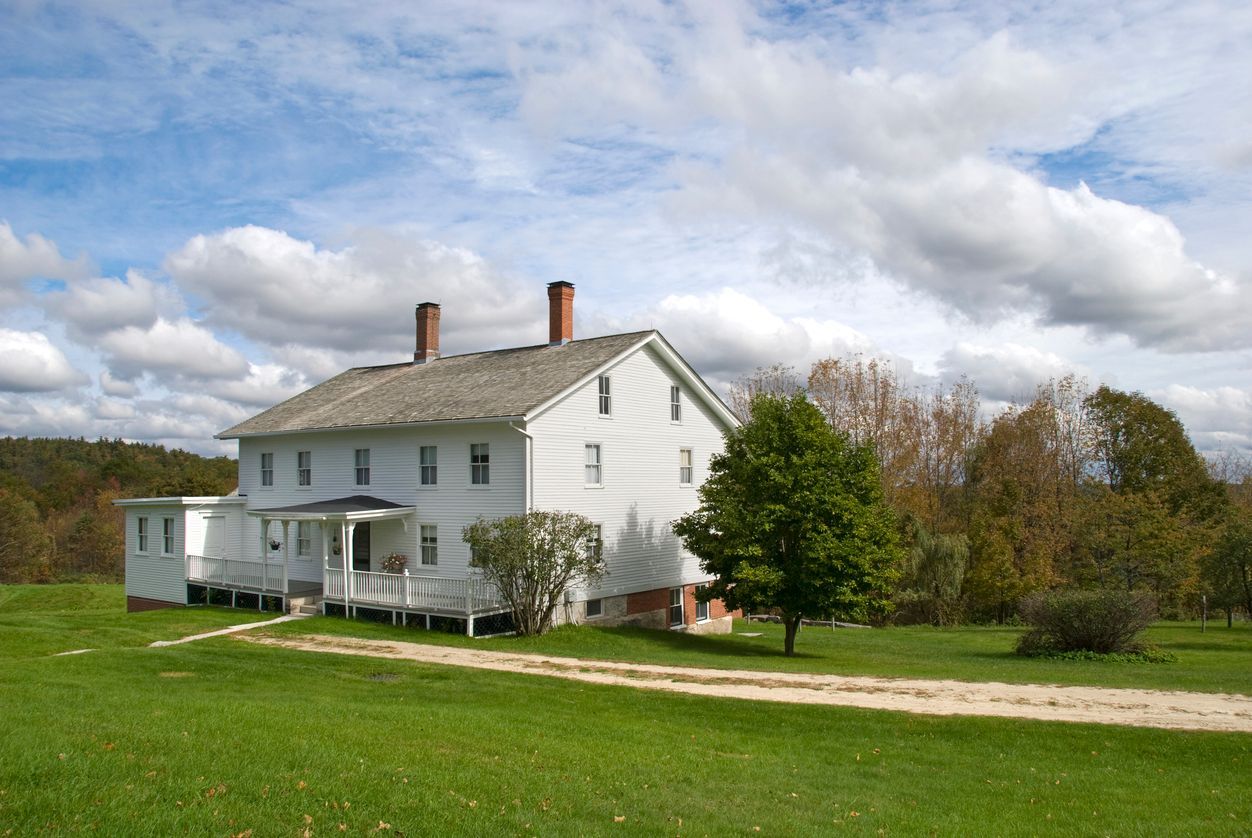 White farmhouse on green lawn under a cloudy sky.