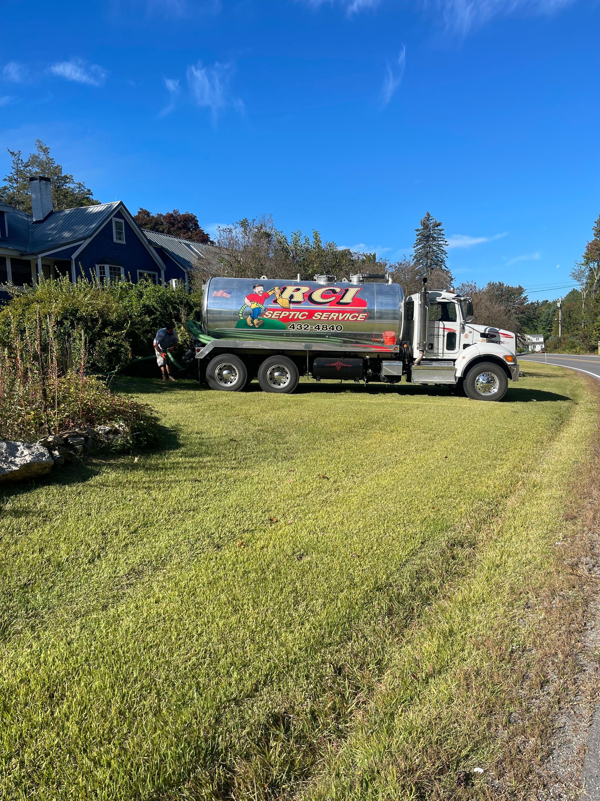 Fuel truck parked on grass next to a blue house; sunny day.