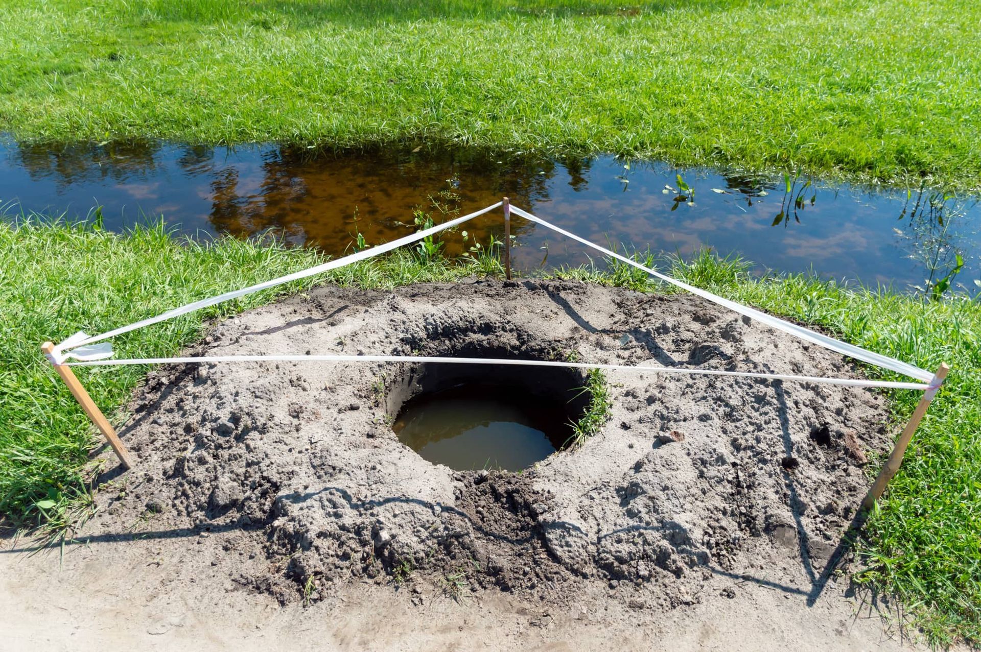 A hole in the ground surrounded by a fence and a puddle of water