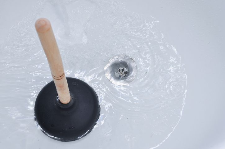 A plunger with a wooden handle is floating in a sink.