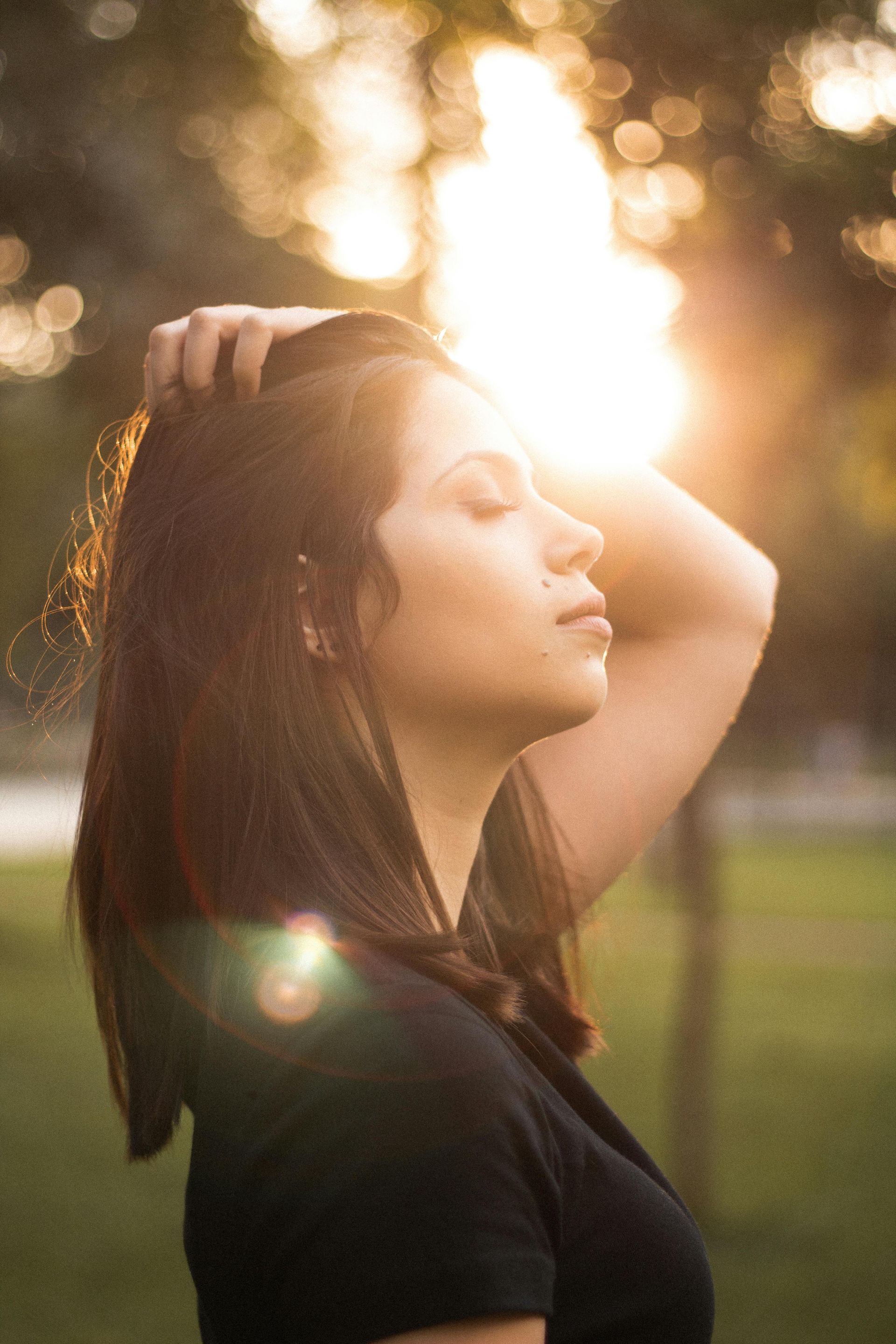 Donna con le mani nei capelli e gli occhi chiusi, che si crogiola al sole.