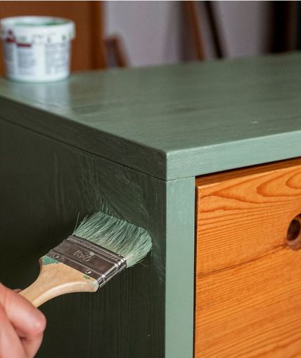 Hand painting a green cabinet with a brush, drawer visible.