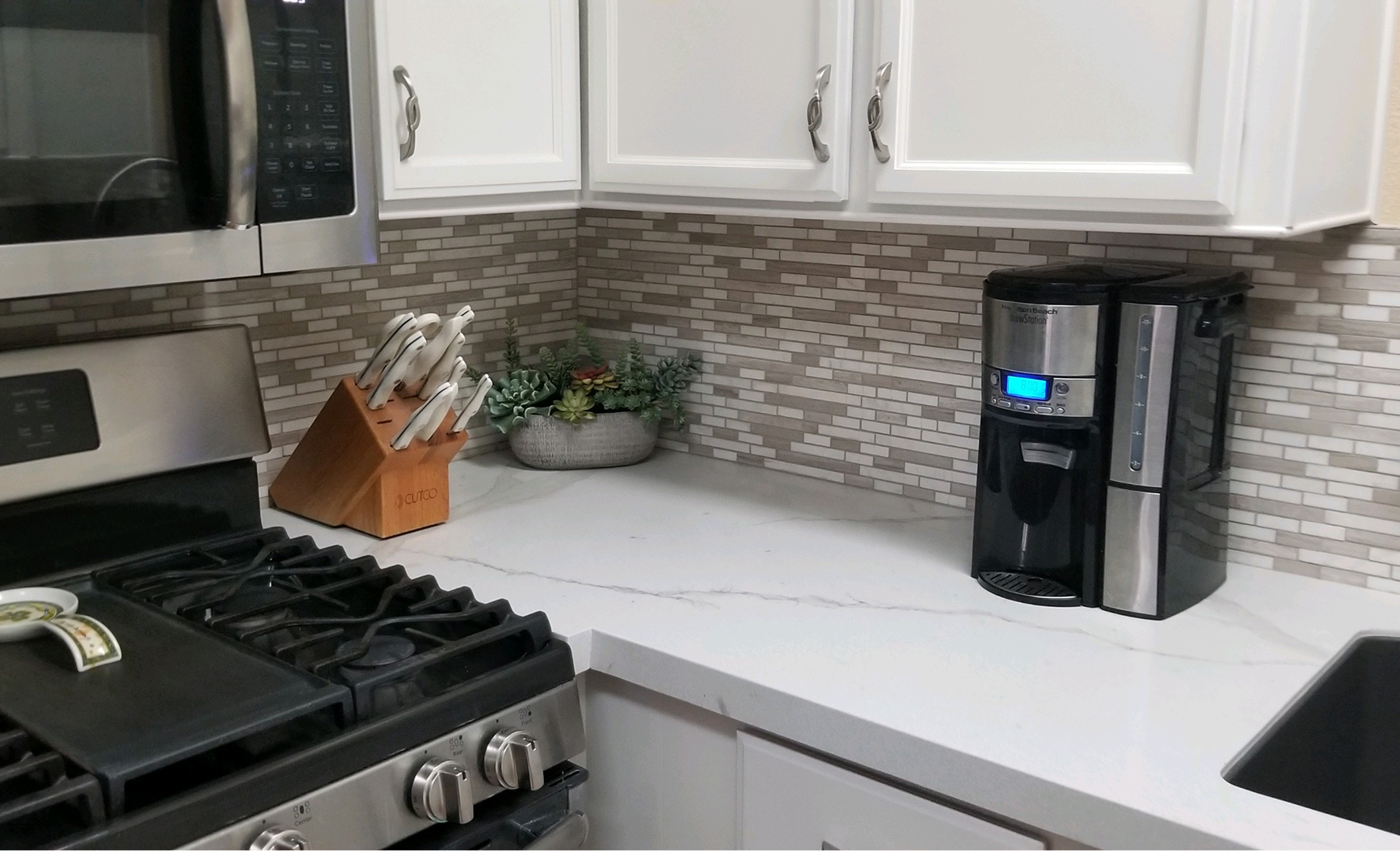 A kitchen with a stove , microwave , coffee maker and sink.