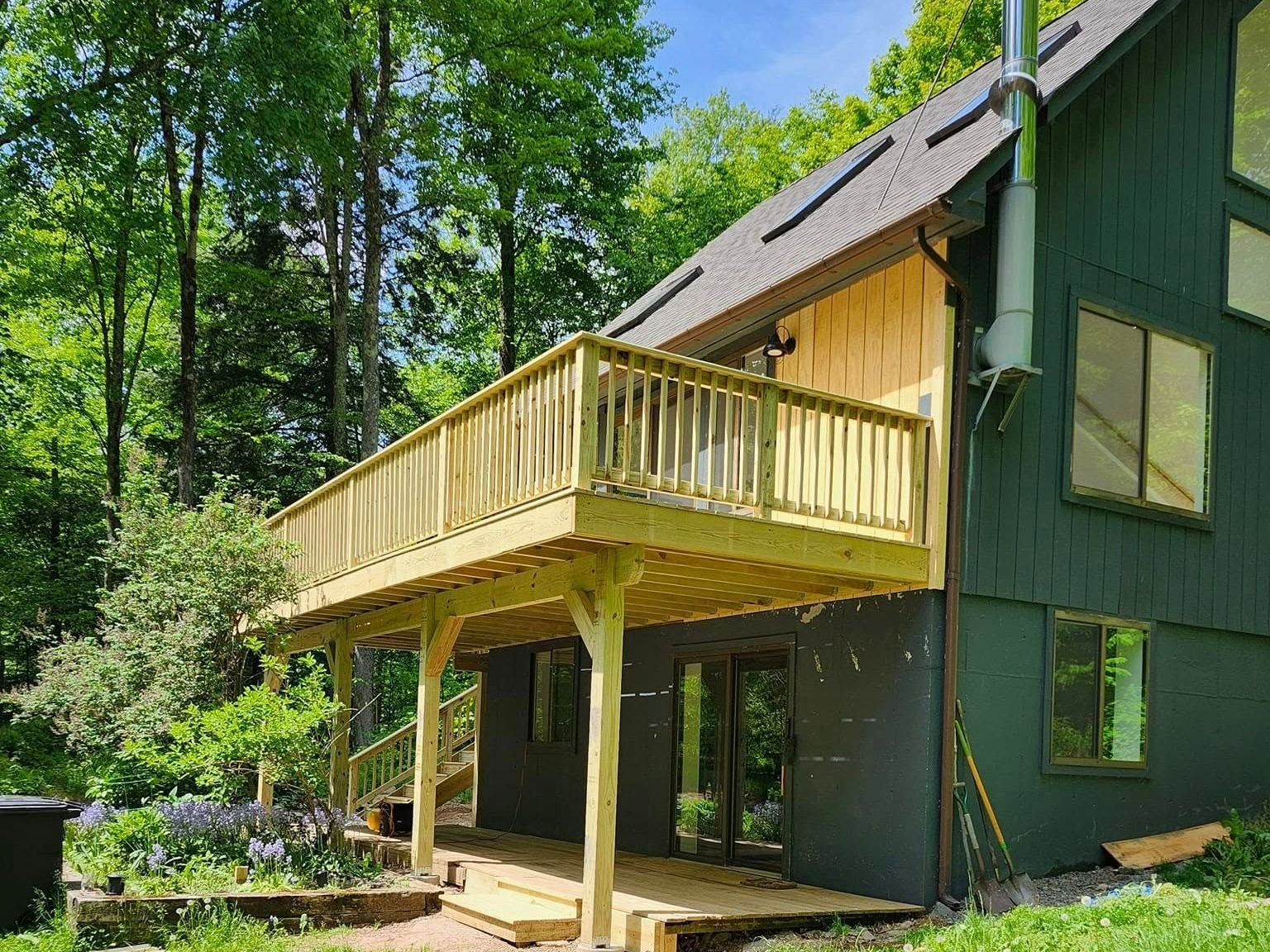 A green house with a wooden deck in front of it.
