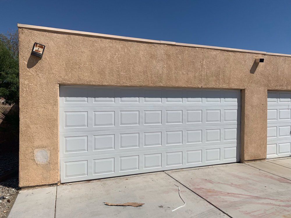 A garage with two white garage doors on a sunny day