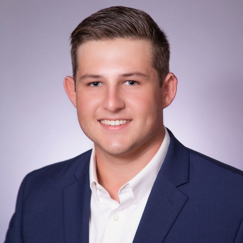 Man in navy blazer and white shirt smiles, headshot.