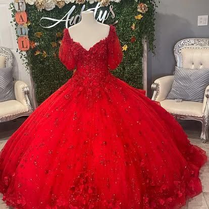A red ball gown with long sleeves is on a mannequin in a room.