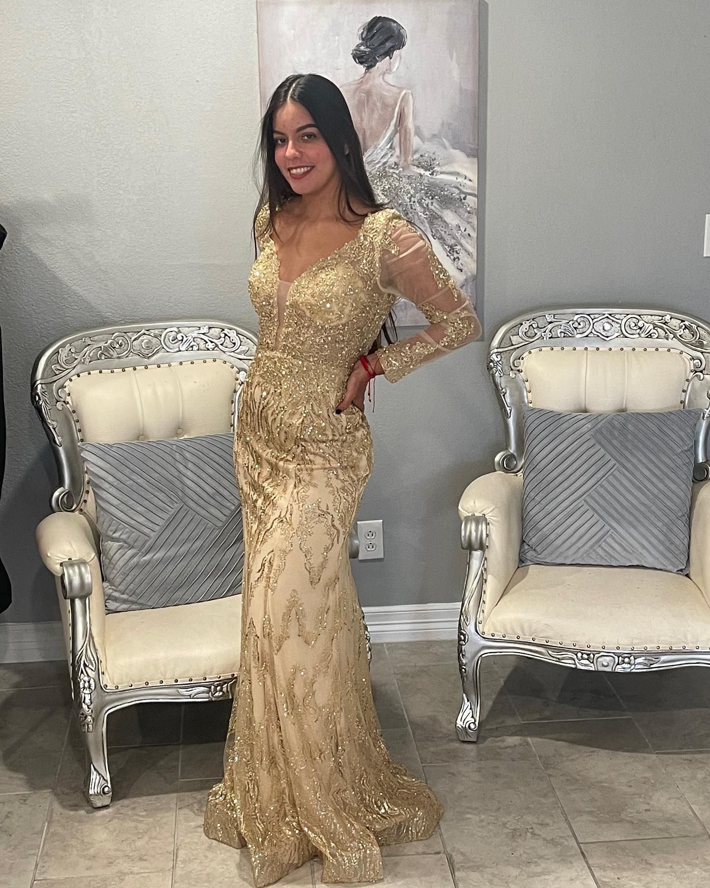 A woman in a gold dress is standing in front of two chairs.